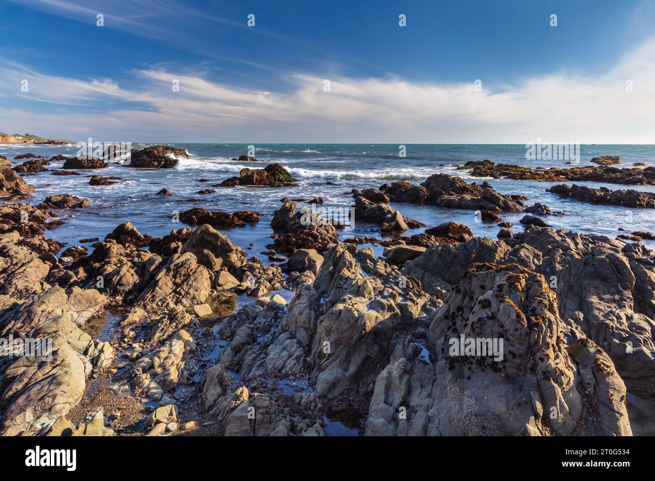 Spiaggia rocciosa con bassa marea a Cambria, California. Oceano Pacifico oltre. Cielo blu, nuvole sullo sfondo. Foto Stock