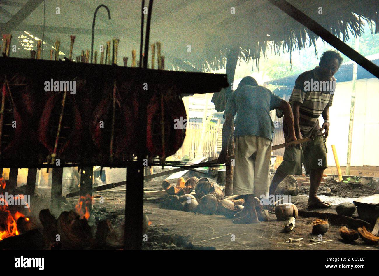 Un lavoratore mantiene la distribuzione equa delle bucce di cocco utilizzate come combustibile per fumare le carni di tonno striato in un'industria domestica a Bitung, Sulawesi settentrionale, Indonesia. I contributi delle popolazioni indigene all'innovazione tecnologica offrono un'ampia gamma di opzioni per la gestione, tra l'altro, della sicurezza alimentare, secondo la relazione del 2023 del gruppo intergovernativo sui cambiamenti climatici (IPCC). Popolarmente conosciuto come cakalang fufu, il tonno affumicato è considerato un cibo esotico indigeno, una parte della produzione di tonno striato che è una delle attività economiche più importanti della città di Bitung. Foto Stock