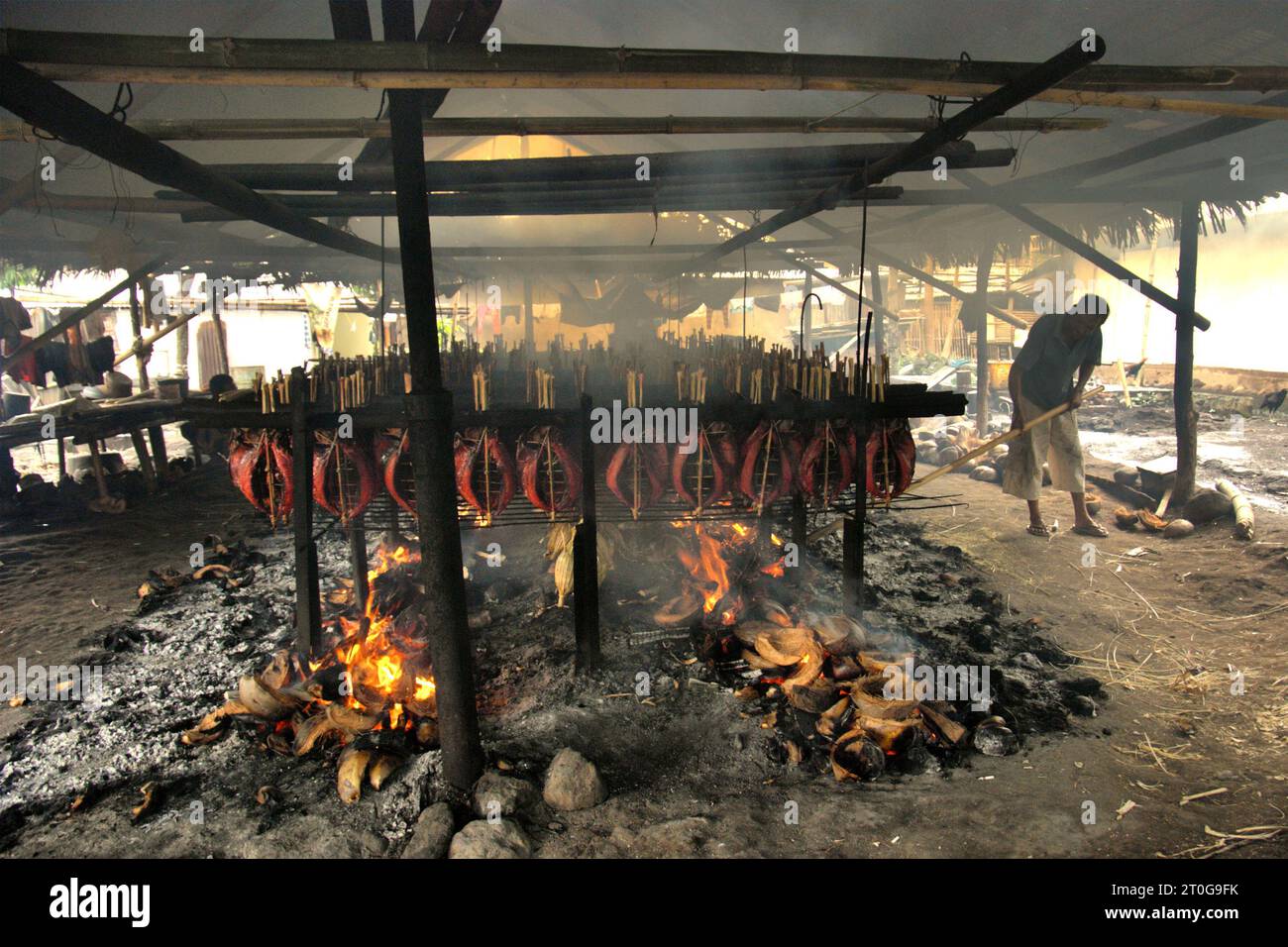 Un lavoratore mantiene la distribuzione equa delle bucce di cocco utilizzate come combustibile per fumare le carni di tonno striato in un'industria domestica a Bitung, Sulawesi settentrionale, Indonesia. I contributi delle popolazioni indigene all'innovazione tecnologica offrono un'ampia gamma di opzioni per la gestione, tra l'altro, della sicurezza alimentare, secondo la relazione del 2023 del gruppo intergovernativo sui cambiamenti climatici (IPCC). Popolarmente conosciuto come cakalang fufu, il tonno affumicato è considerato un cibo esotico indigeno, una parte della produzione di tonno striato che è una delle attività economiche più importanti della città di Bitung. Foto Stock