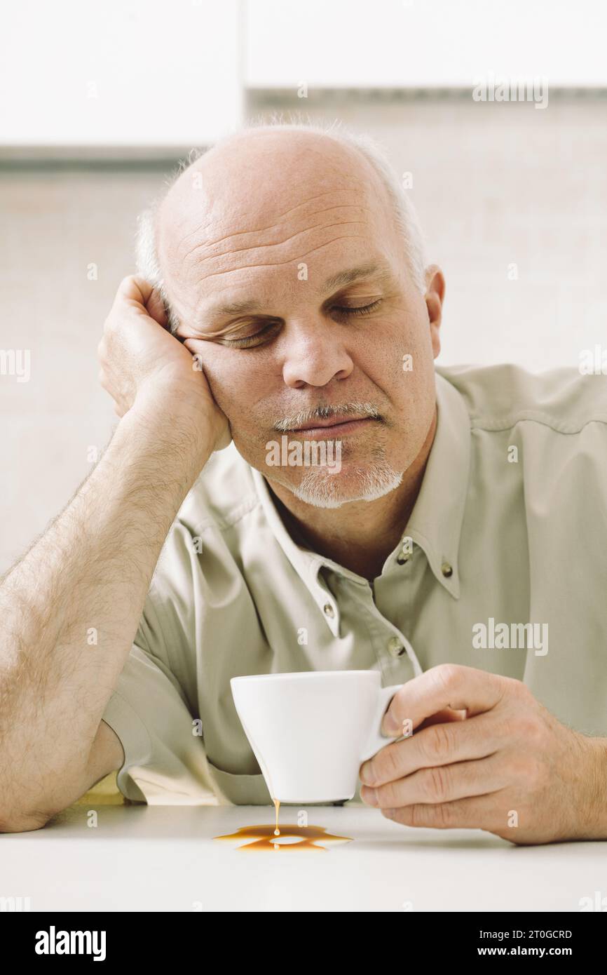 Un uomo anziano, stanco dal risveglio, lotta con il suo caffè mattutino. La privazione del sonno influisce sul suo lavoro. L'età pensionabile aumenta, ma non il suo stipendio. Medi Foto Stock