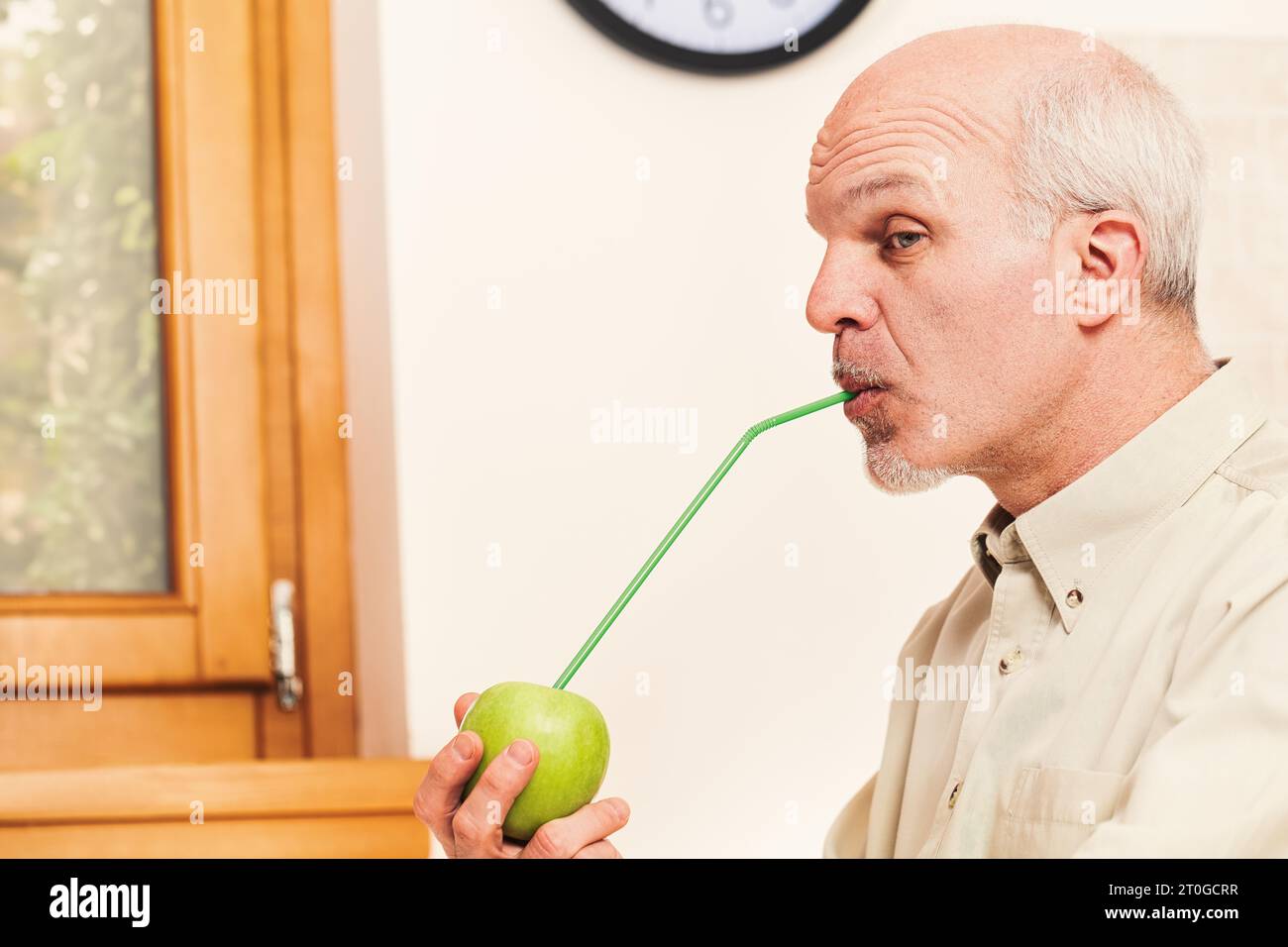 Nella sua cucina, un anziano malizioso e giocoso allegra ogni vitamina da una mela verde. Mentre scherza, crede fermamente nell'adagio e nell'importa Foto Stock