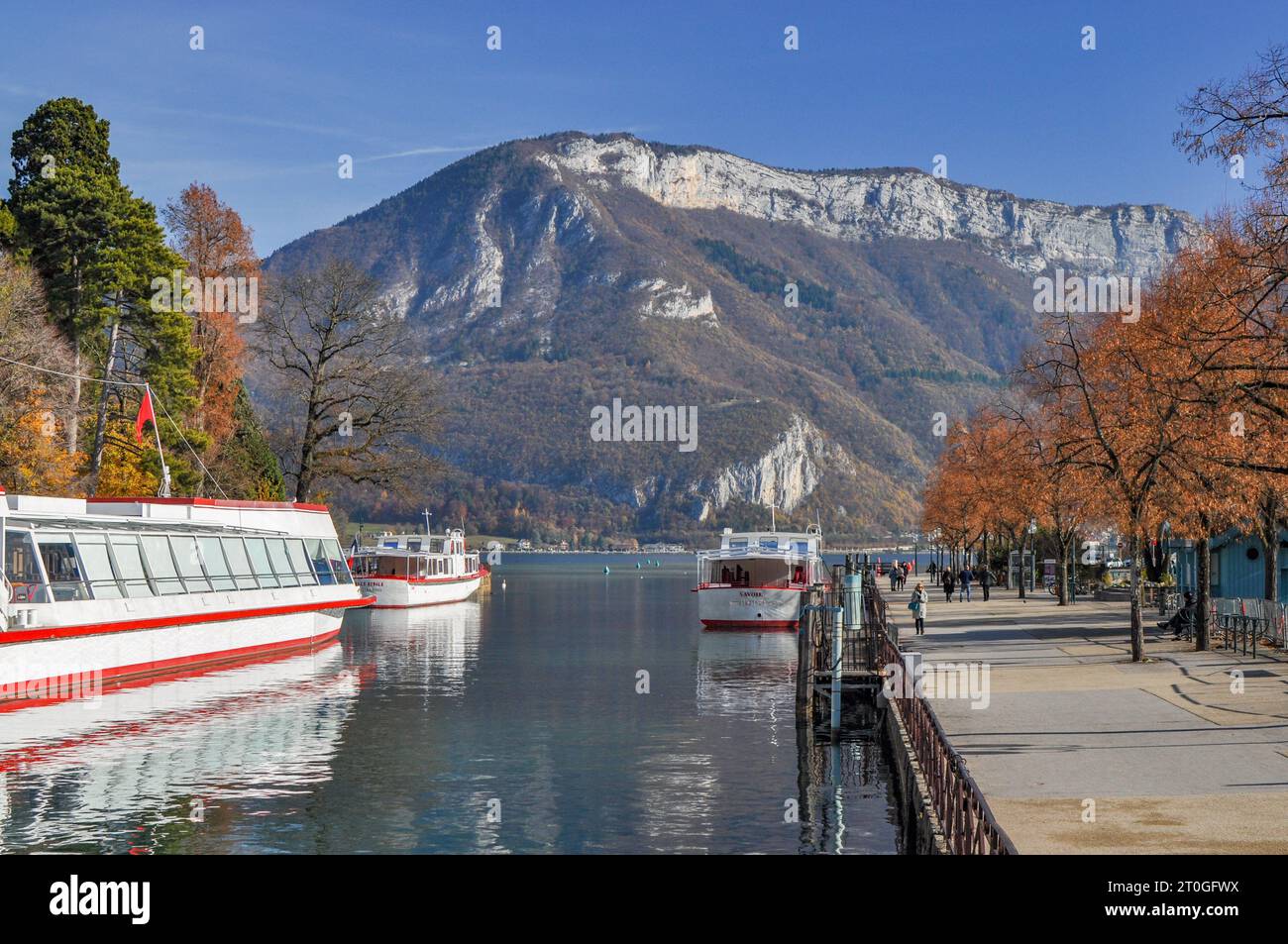 Il fiume Thiou sfocia nel lago di Annecy in Francia, con barche e una catena montuosa sullo sfondo in autunno Foto Stock