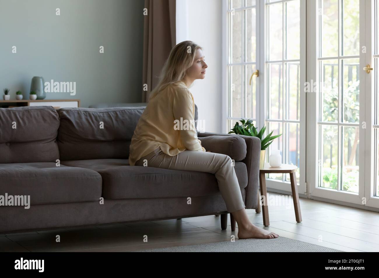 Graziosa giovane donna seduta su un divano al chiuso, Foto Stock