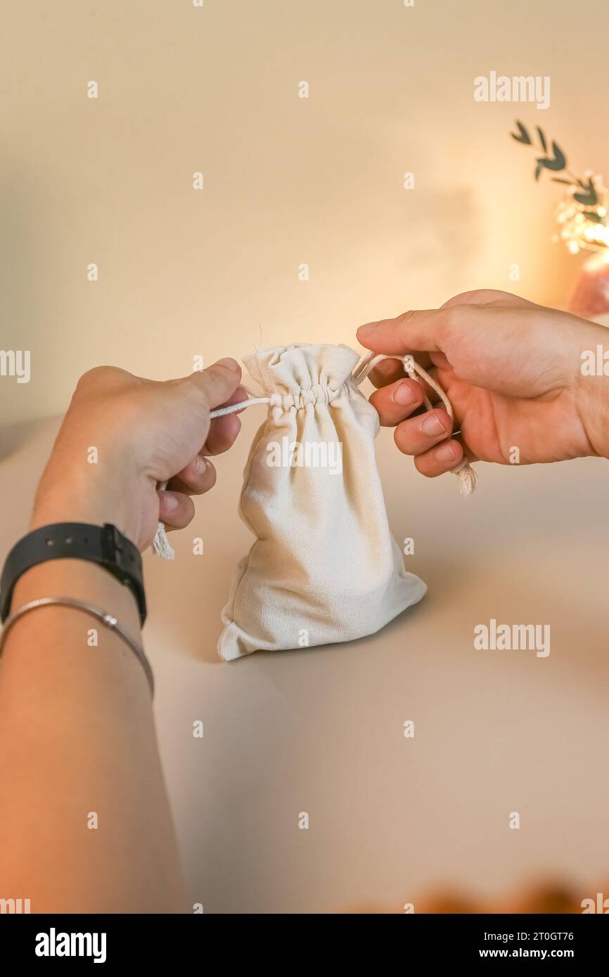 Apertura delle mani, borsa con coulisse in tela, mockup in moschettone con cubo di legno per un design o una presentazione di testo personalizzata Foto Stock