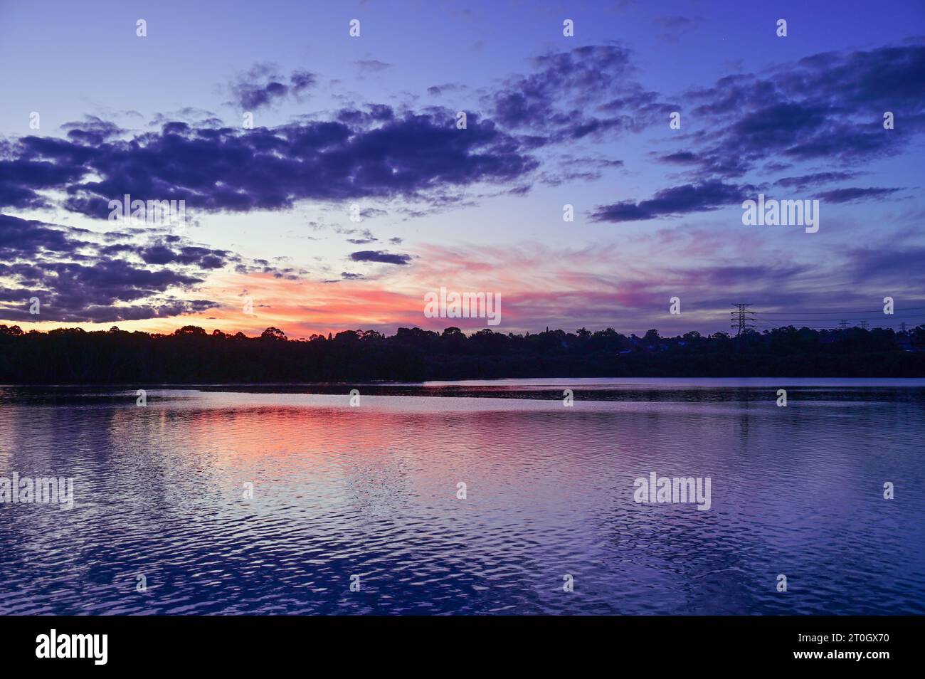 Vista sul fiume dopo il tramonto con riflessione della luce residua e l’ora blu che cala con nuvole grigie nel cielo. Parramatta River, Newington, Sydney, Australia Foto Stock