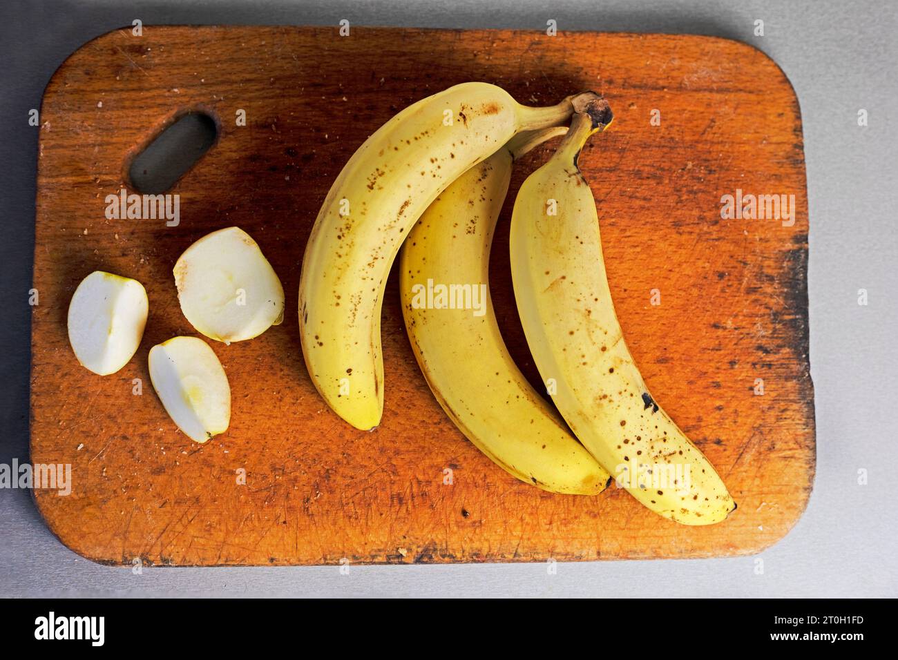 mazzo di banane con fette di mela su un tagliere di legno su sfondo grigio. flatlay Foto Stock