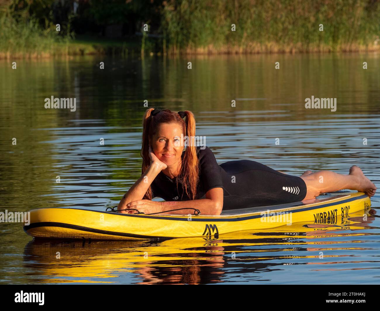 Donna sdraiata su una tavola da paddle a standup nel lago, in Germania Foto Stock