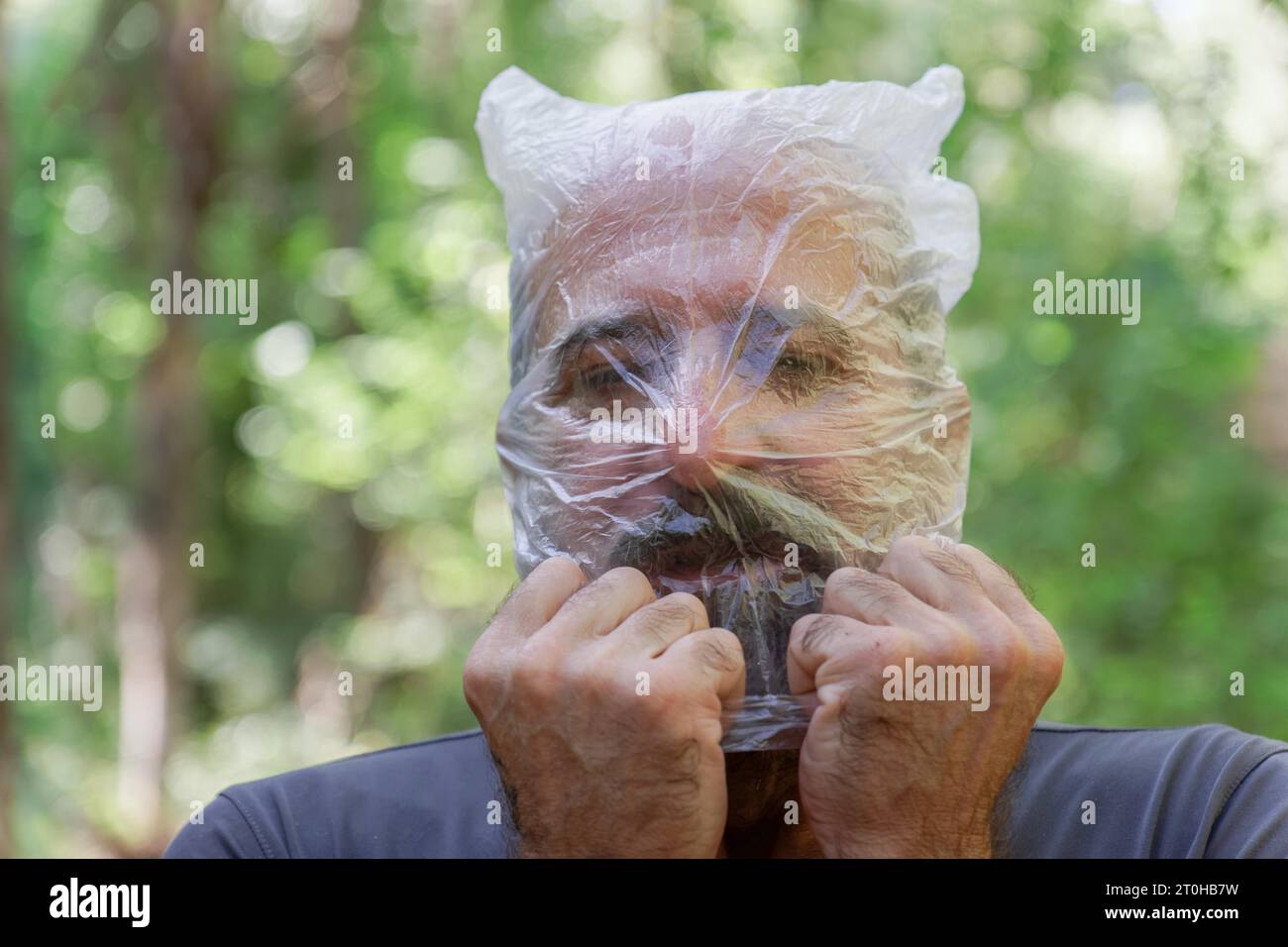 Uomo con un sacchetto di plastica sulla testa che annegava in campagna, riciclando il concetto di ecologia Foto Stock