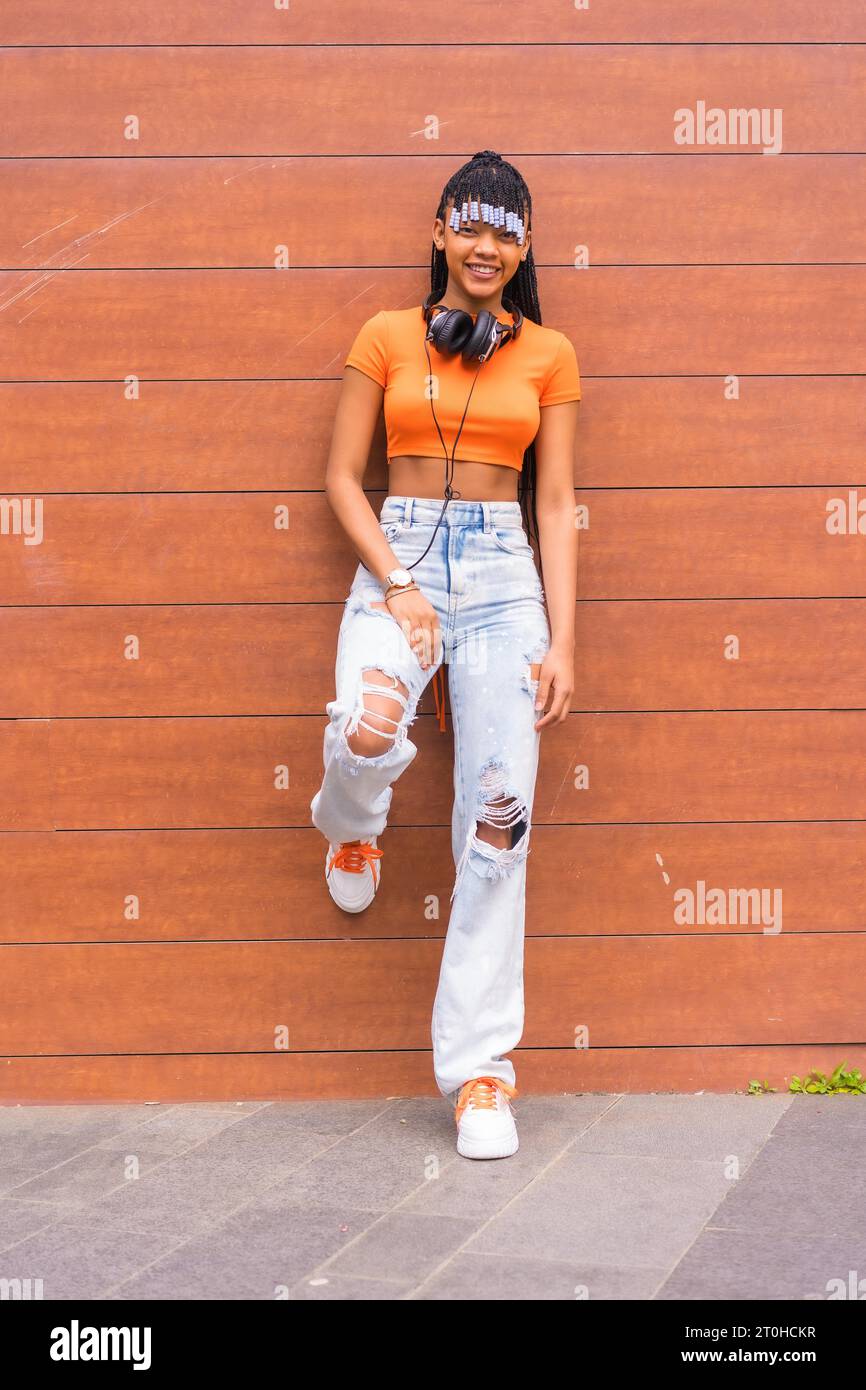 Stile di vita con una giovane ballerina in trappola in città. Ragazza di razza nera del gruppo etnico africano con maglietta arancione e pantaloni da cowboy Foto Stock