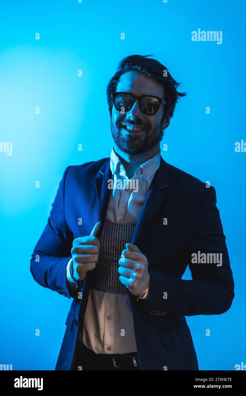Studio Lifestyle, un bel giovane uomo caucasico in una sessione con abiti eleganti e occhiali da sole, con luce blu neon Foto Stock