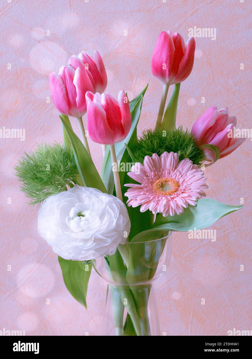 Un piccolo vaso in ceramica bianca che regge un bouquet vibrante e colorato di fiori e fogliame rosa e verde Foto Stock