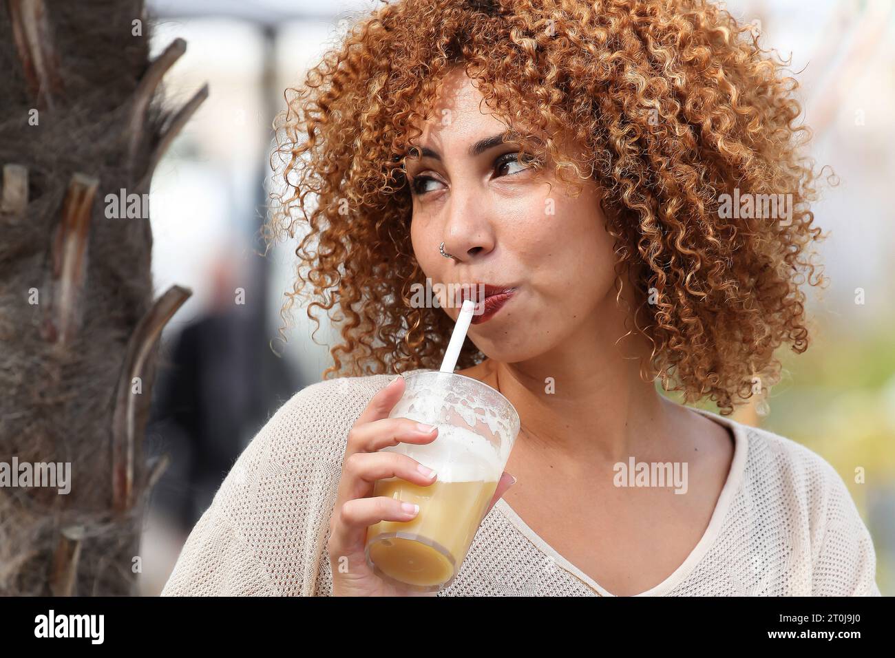 Ritratto di una donna dai capelli ricci che beve all'aperto in un paese esotico Foto Stock