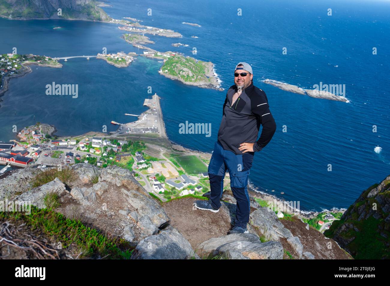 Rilassato e felice escursionista gode di una vista mozzafiato sulle cime di Reinebringen delle isole Lofoten, dei fiordi e della Norvegia Foto Stock
