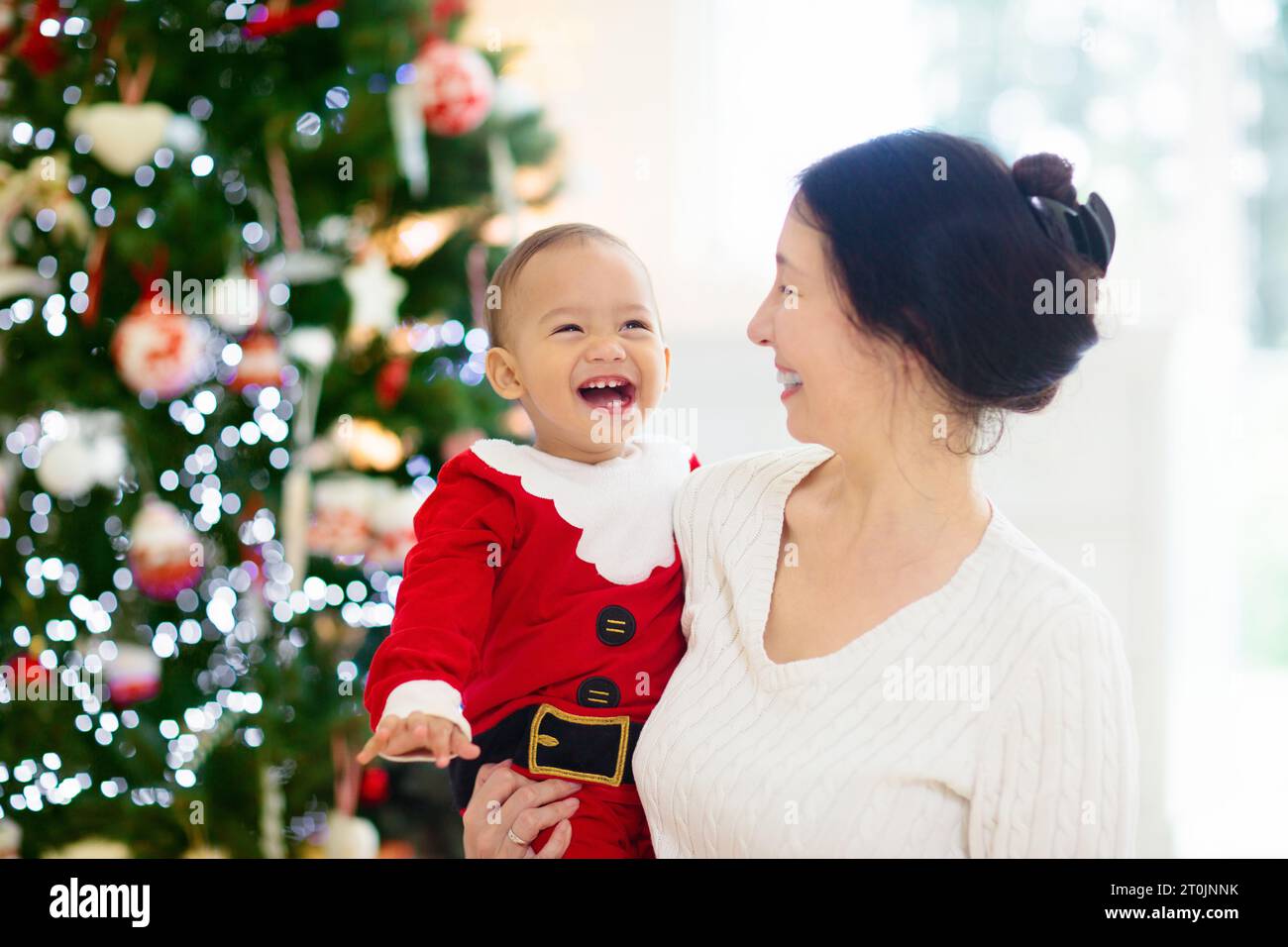 Famiglia asiatica con bambini all'albero di Natale e caminetto. Madre e bambini aprono regali al caminetto. Baby e mamma aprono i regali. Vacanze invernali Foto Stock