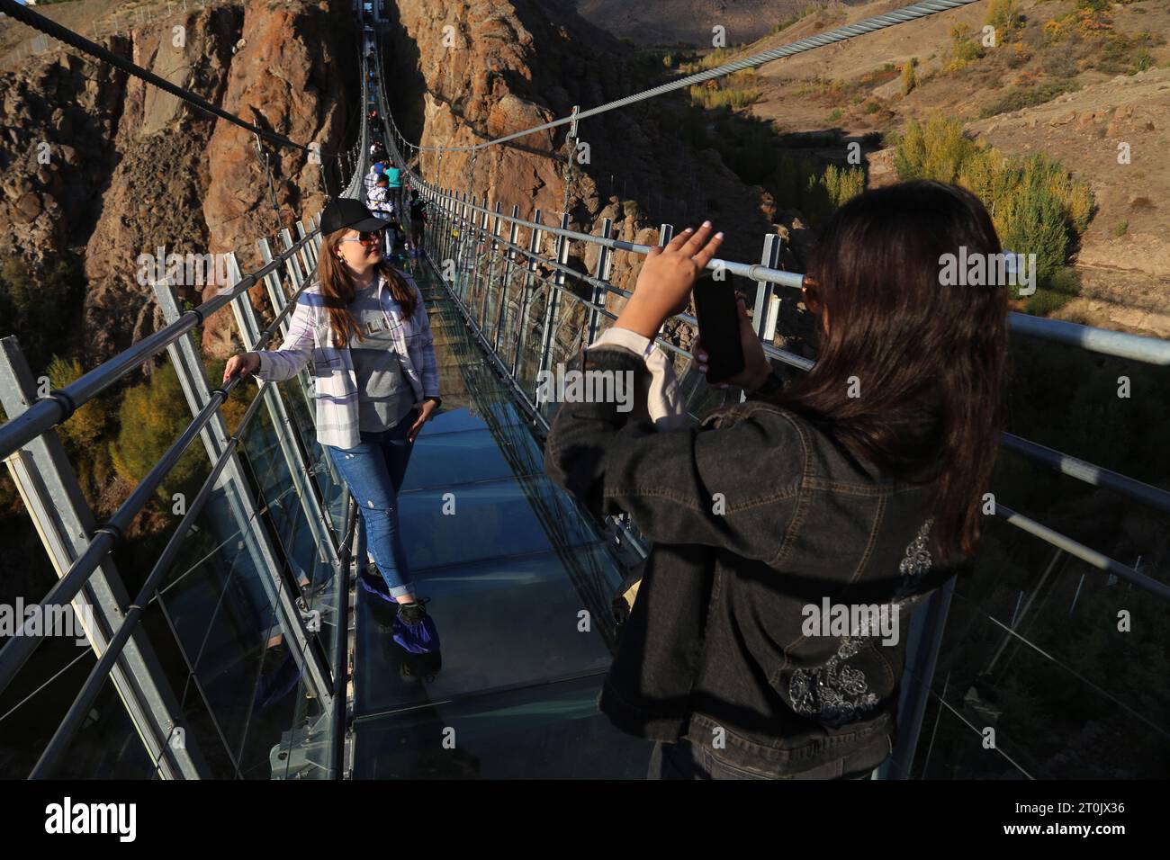 Hir, Ardabil, Iran. 5 ottobre 2023. Una donna iraniana senza coprire il suo velo islamico obbligatorio scatta una foto sul ponte sospeso in vetro ad arco nell'area ricreativa di Hir vicino alla città di Ardabil. Con i suoi 208 metri di lunghezza, 1,5 metri di larghezza e 100 metri di altezza, il ponte è un luogo frequentato dai turisti. (Immagine di credito: © Rouzbeh Fouladi/ZUMA Press Wire) SOLO USO EDITORIALE! Non per USO commerciale! Foto Stock