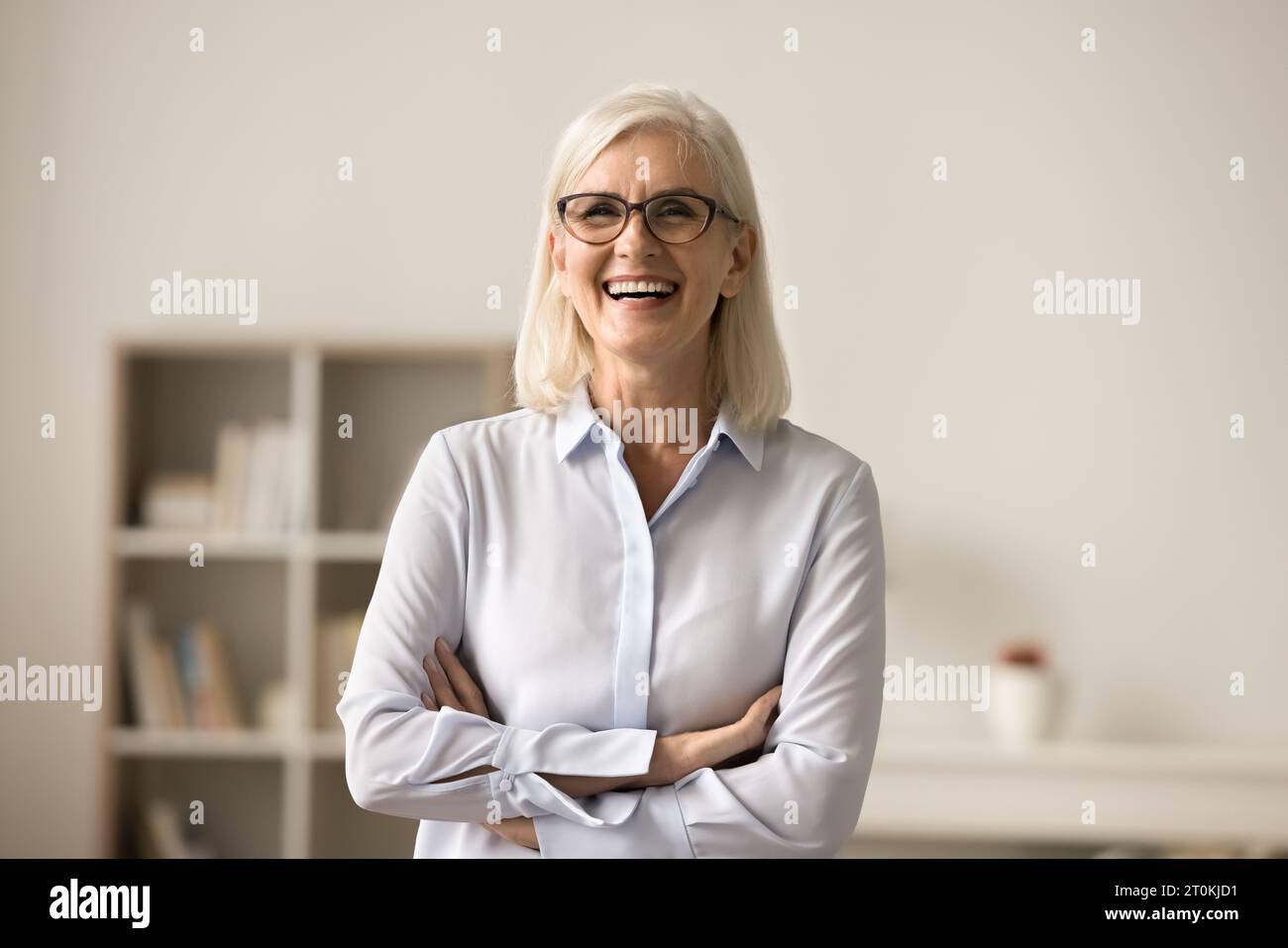Donna d'affari anziana, allegra e sicura, con occhiali eleganti in posa in interni Foto Stock