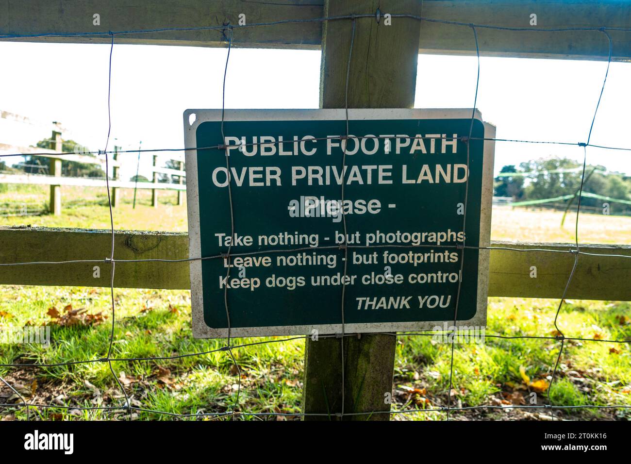 Un cartello verde attaccato a una recinzione di legno che indica le regole per camminare lungo un sentiero pubblico su un terreno privato Foto Stock