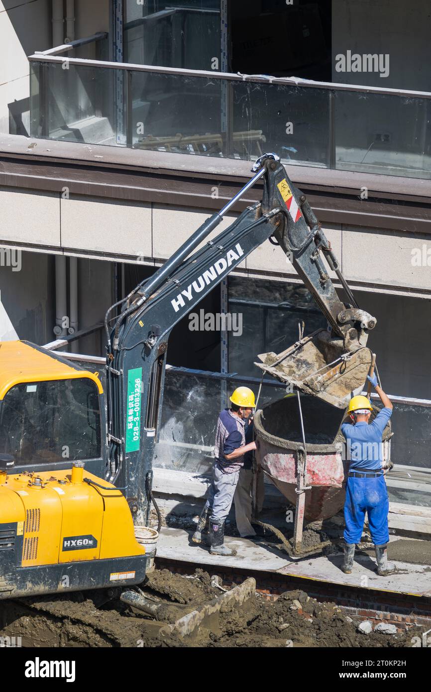 In una giornata di sole, un gruppo di operai edili sta scaricando cemento pre-miscelato portato da un carrello elevatore vicino all'edificio in costruzione. Foto Stock