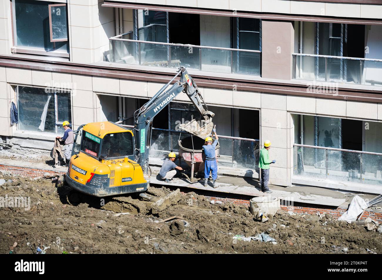 In una giornata di sole, un gruppo di operai edili sta scaricando cemento pre-miscelato portato da un carrello elevatore vicino all'edificio in costruzione. Foto Stock