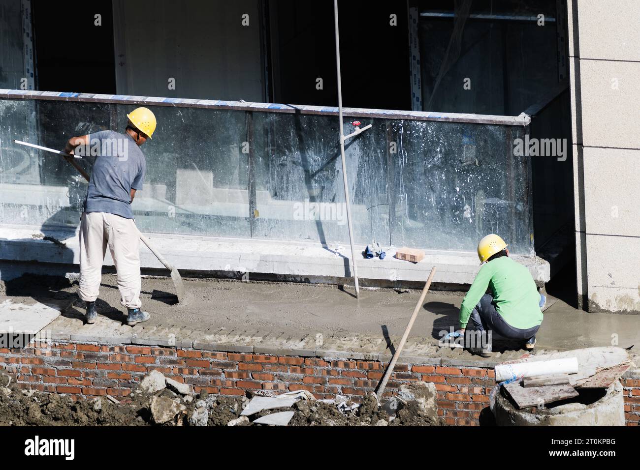 In una giornata di sole, gli operai edili stanno posando cemento per la strada accanto all'edificio residenziale in costruzione. Foto Stock