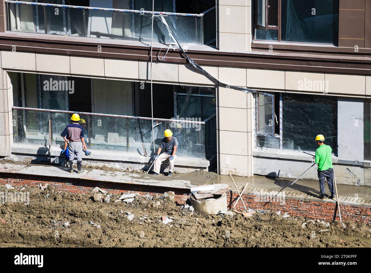 Alcuni lavoratori stanno riposando mentre altri stanno ancora lavorando alla costruzione della casa in una giornata di sole. Foto Stock