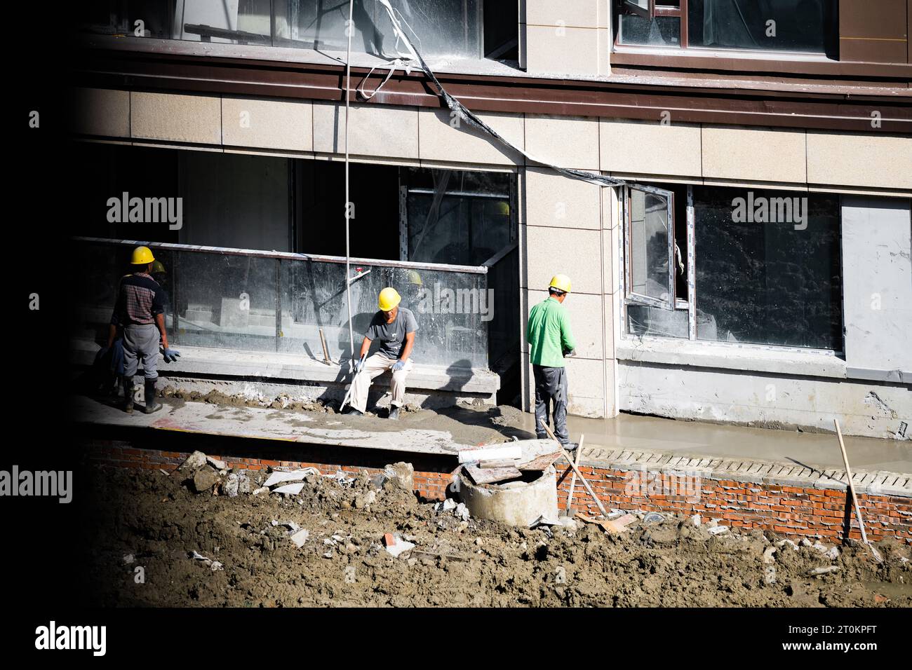Alcuni lavoratori stanno riposando mentre altri stanno ancora lavorando alla costruzione della casa in una giornata di sole. Foto Stock