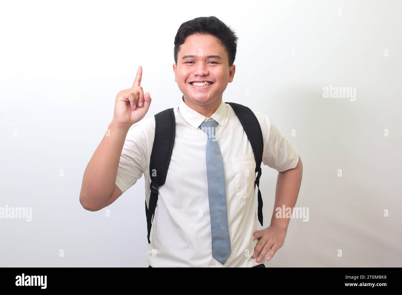 Studente indonesiano delle superiori che indossa un'uniforme bianca con cravatta grigia che punta verso l'alto con il dito e ricorda qualcosa da fare. Immagine isolata Foto Stock