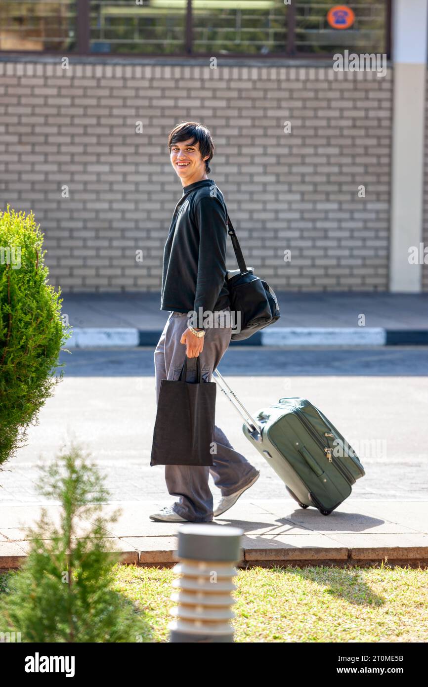 viaggiatore, bel giovane sorridente porta borse davanti all'aeroporto in strada Foto Stock