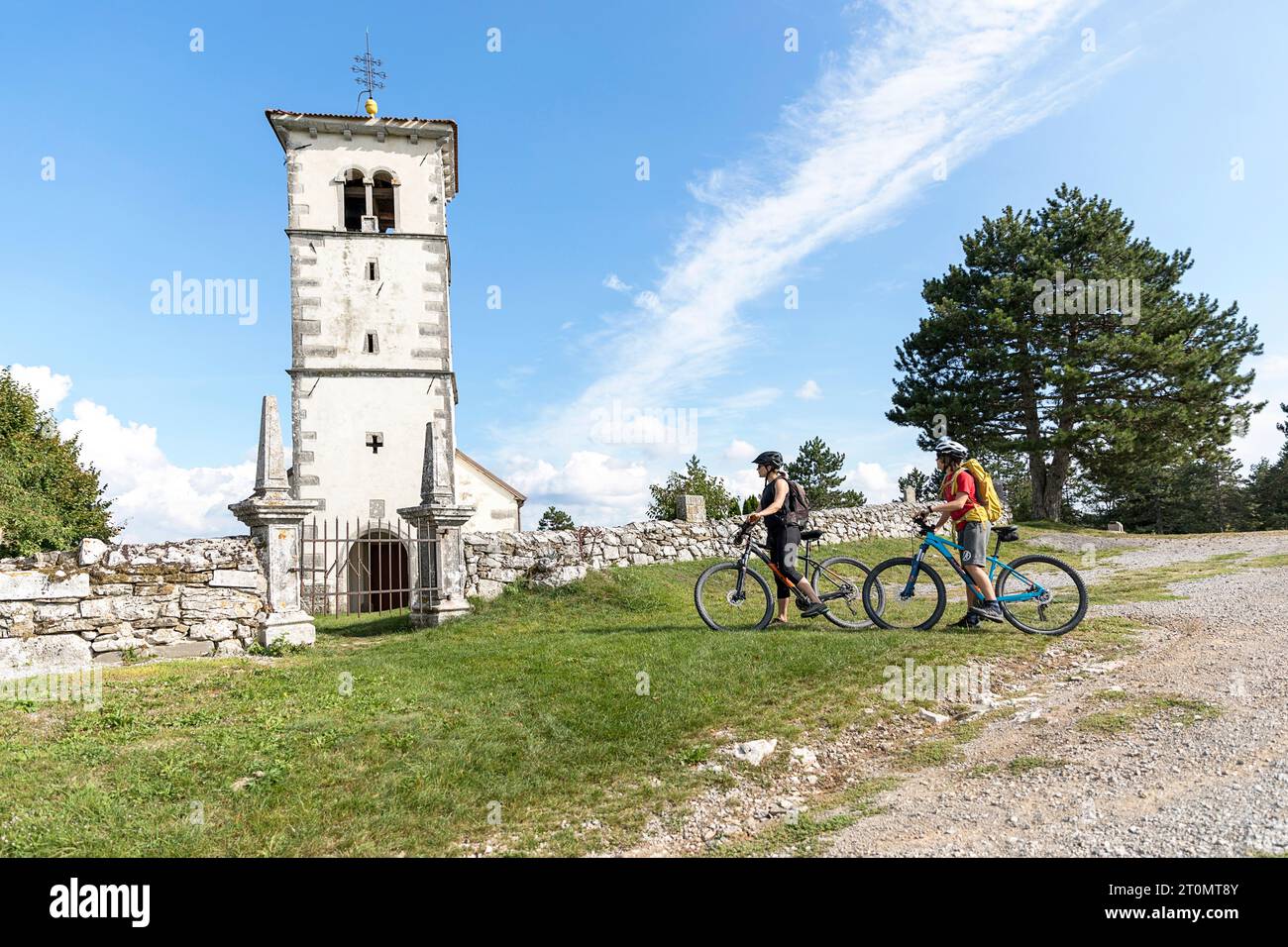 Madre e figlio in una gita in bicicletta con la famiglia in una piccola chiesa di San Martino sopra Pivka nella regione di Notranjska in Slovenia, paesaggio panoramico in una giornata di sole Foto Stock