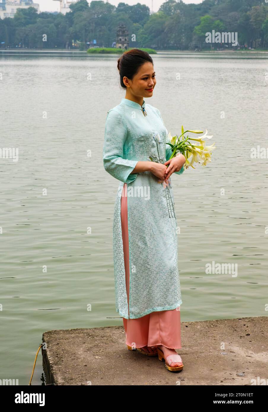 Hanoi, Vietnam. Giovane donna che indossa un Ao dai al lago Hoan Kiem. Foto Stock