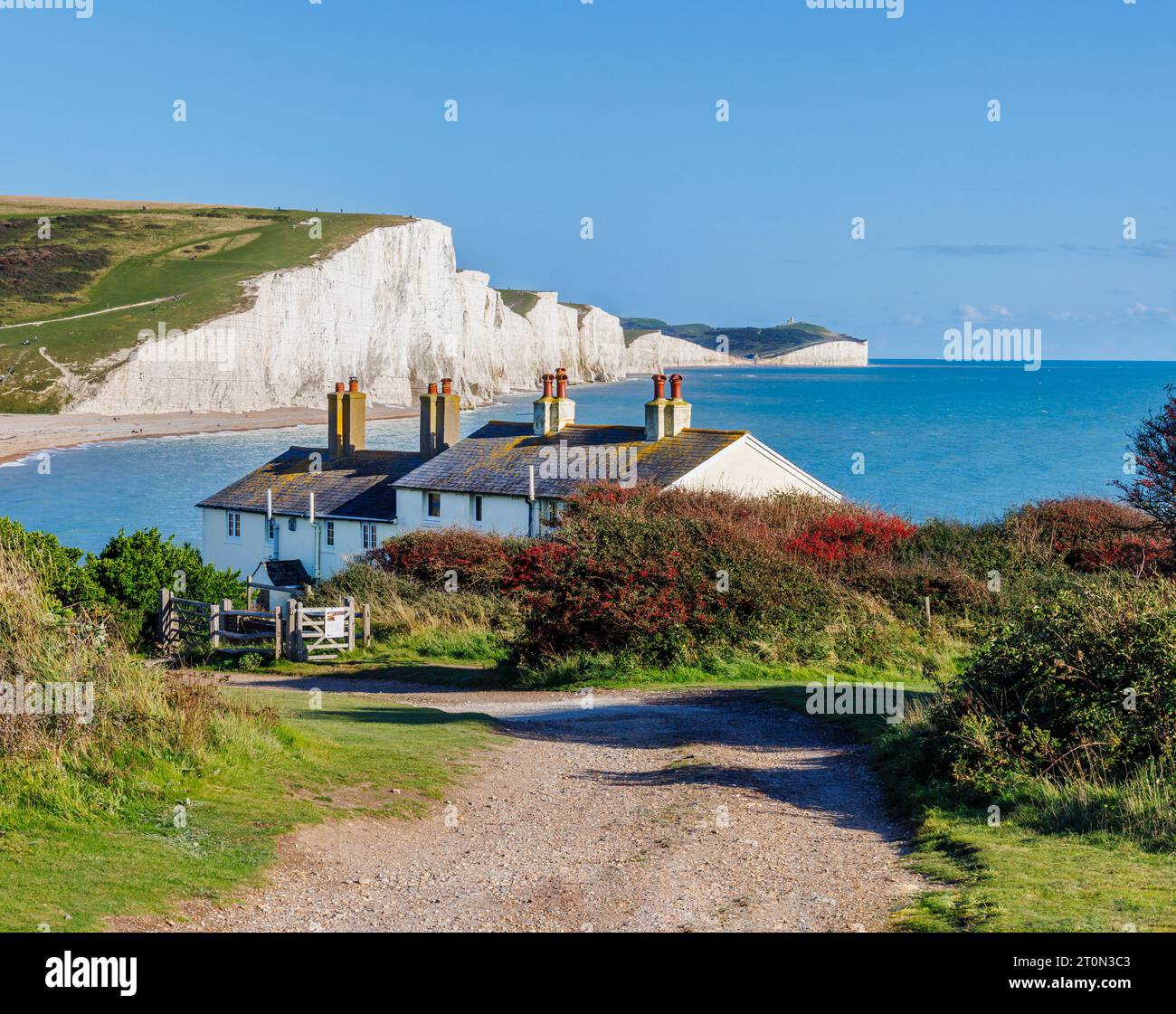 Vista delle scogliere di gesso delle sette Sorelle e dei cottage della guardia costiera da Seaford Head attraverso Cuckmere Haven guardando ad est in una giornata di sole con un cielo blu Foto Stock