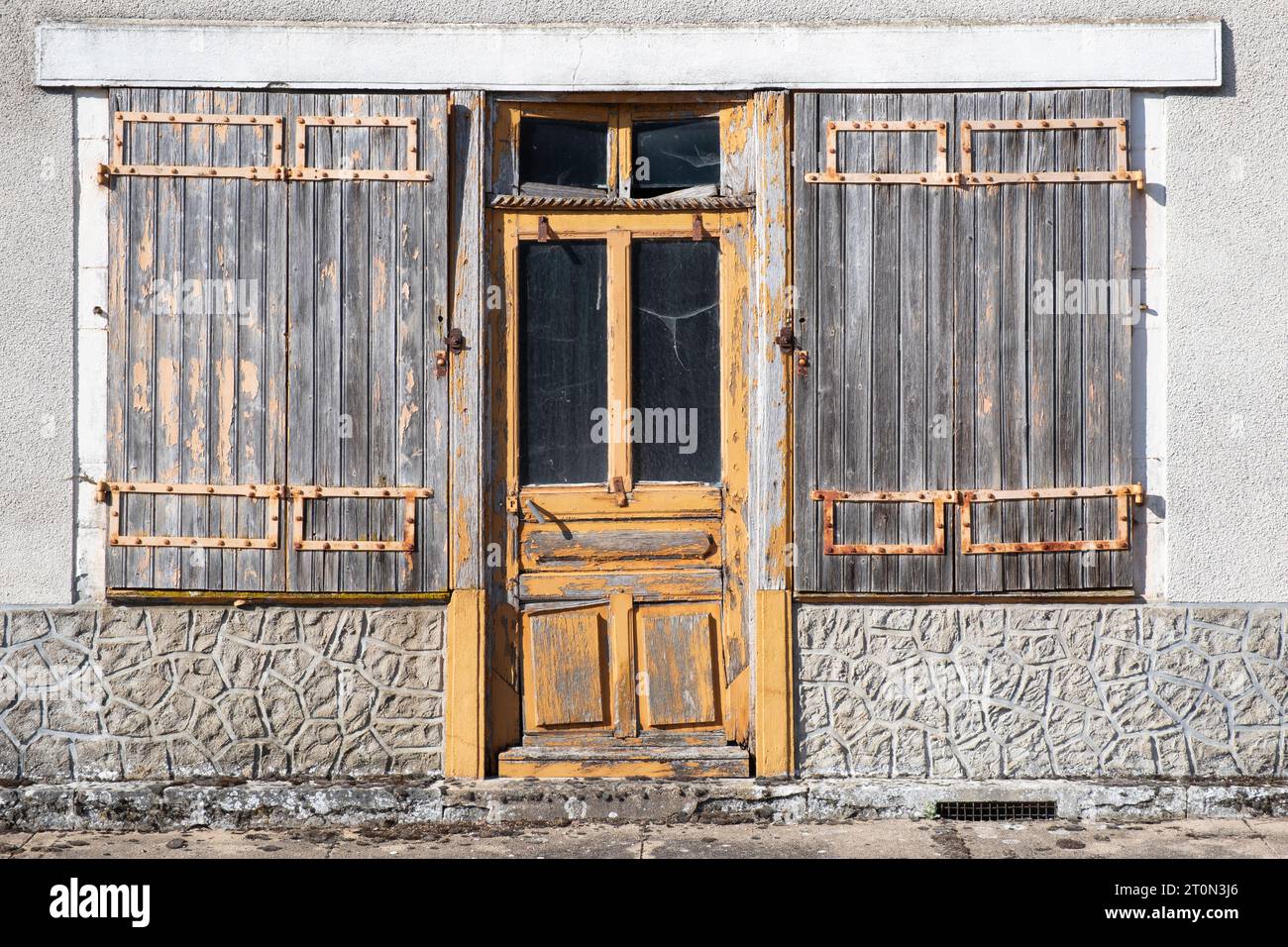 Vecchia porta in legno dipinta di giallo con vetrate laterali e vecchie persiane di legno davanti, in una casa fatiscente, Francia Foto Stock