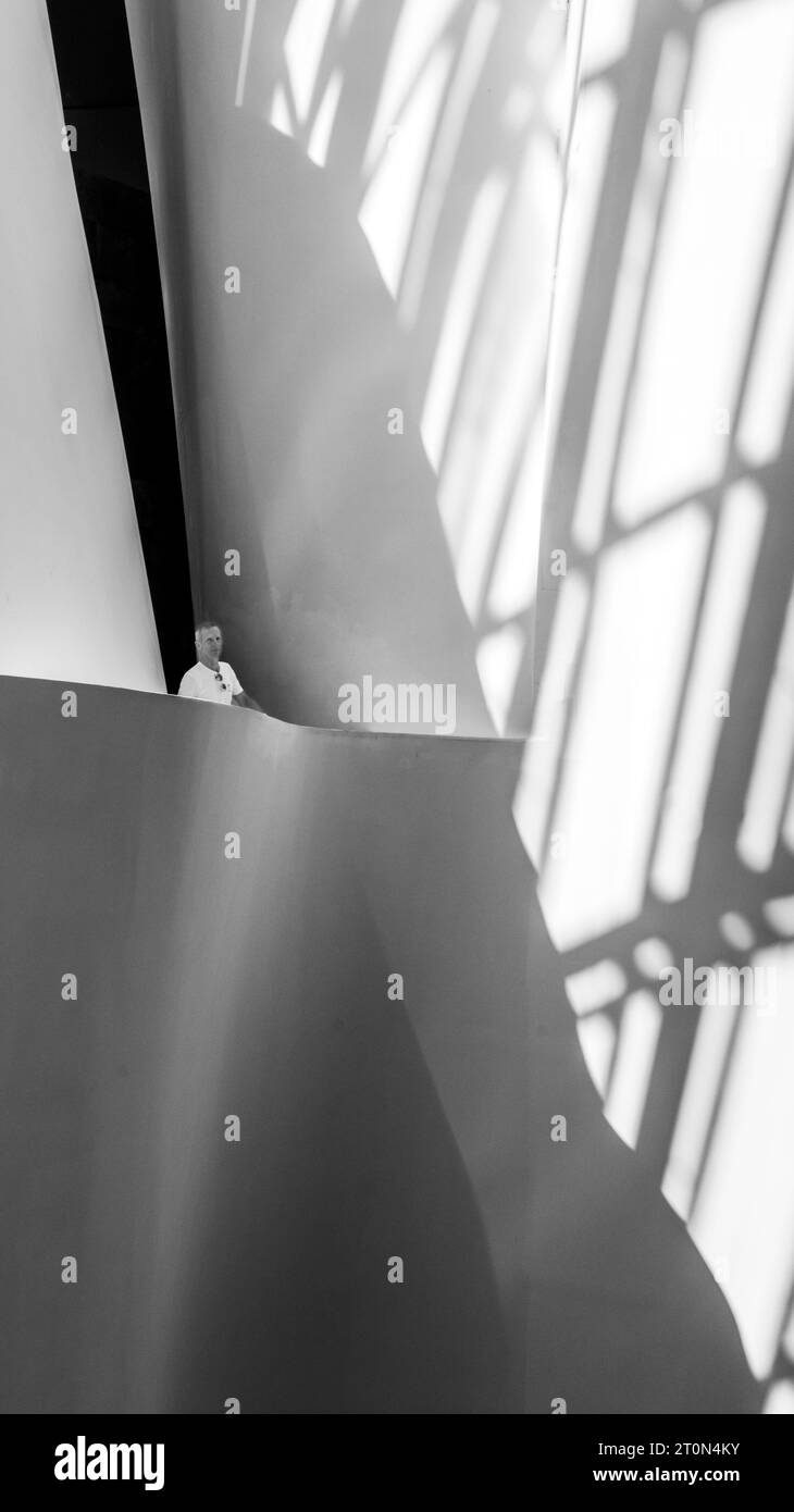 Un uomo in piedi nel mezzo di un edificio moderno con una griglia di ombre sul muro dietro di lui Foto Stock