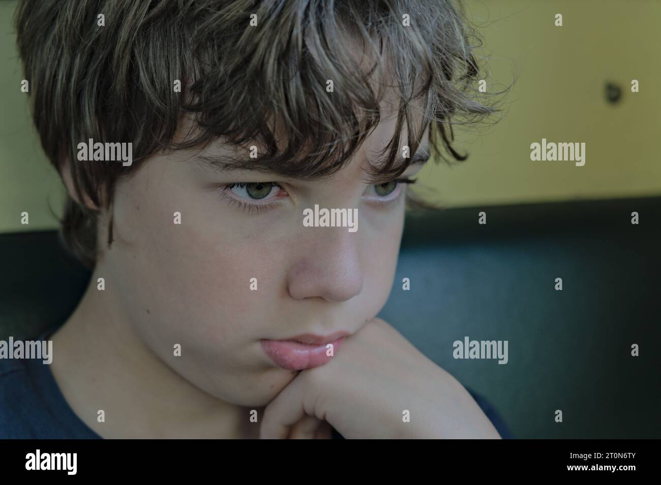 Primo piano ritratto bambino seduto da solo e guardando avanti, pugno sotto il mento di scolaro concetto di pensiero facciale serio ed emotivo Foto Stock