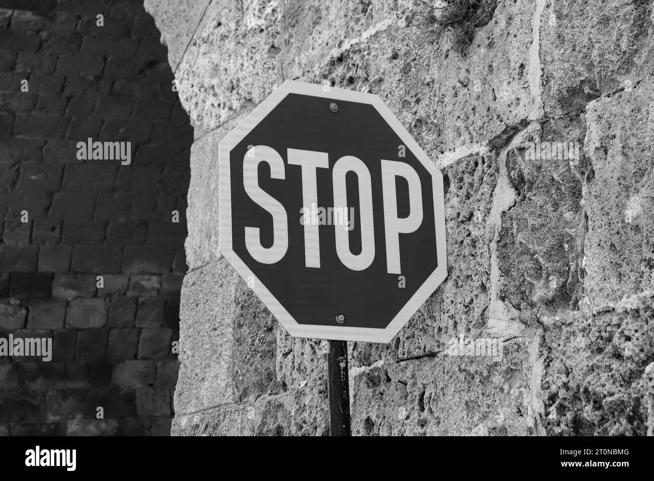 Segnale di stop bianco e nero su un palo contro un muro di pietra di mattoni. Concetto di comunicazione e sicurezza Foto Stock