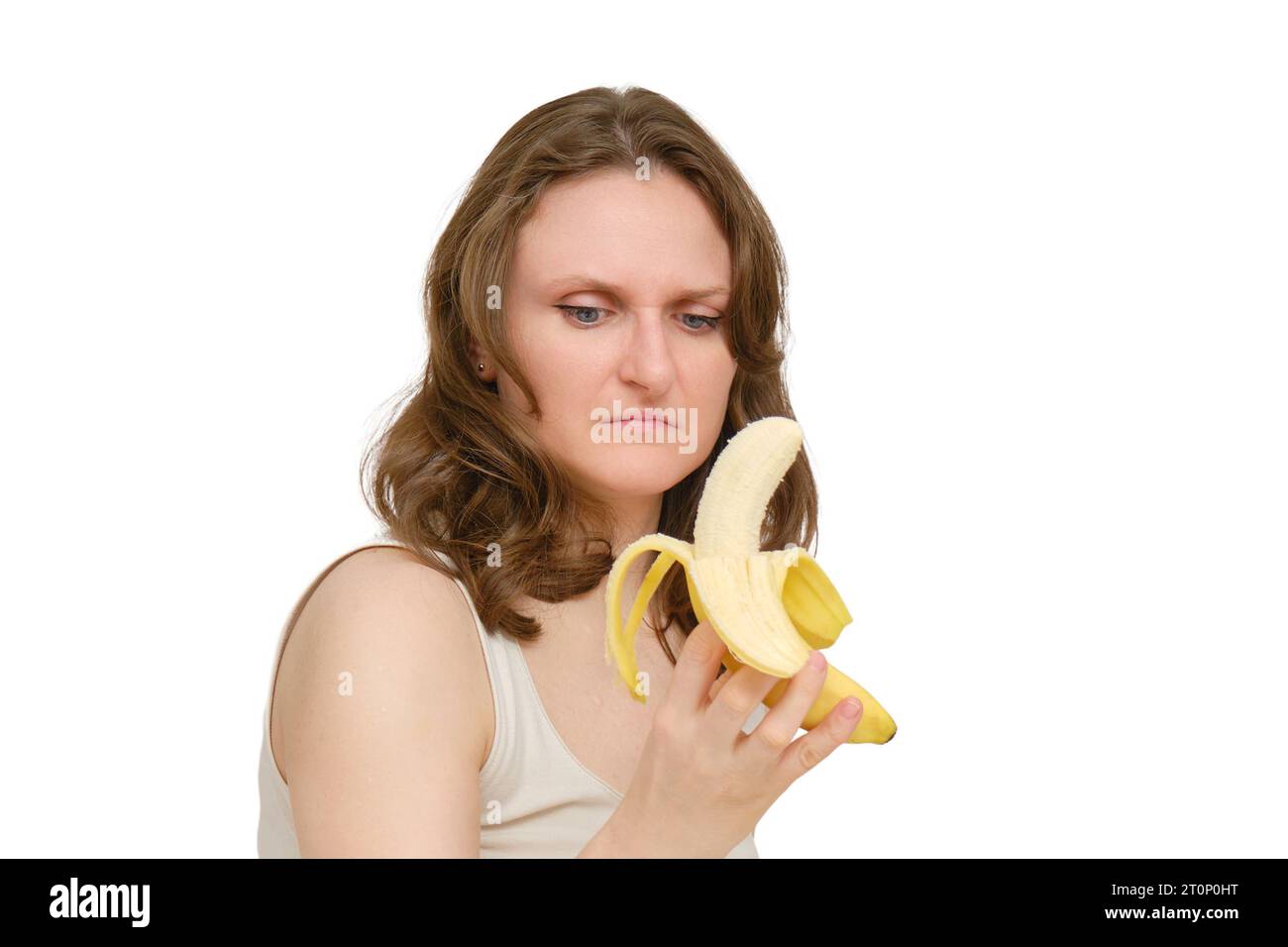 Una donna con dubbi e disprezzo guarda una banana, uno studio, isolato su sfondo bianco. Uno sguardo disgustato al frutto della banana nelle mani di una donna Foto Stock