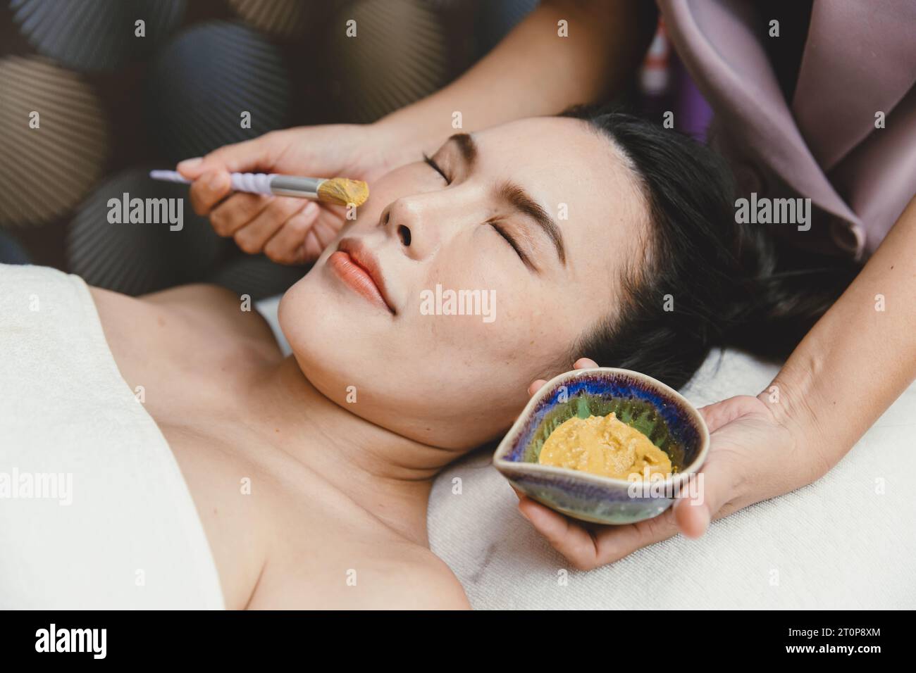 Donna asiatica in salone spa massaggio viso applicando maschera cura della pelle a base di erbe per la bellezza del viso Foto Stock