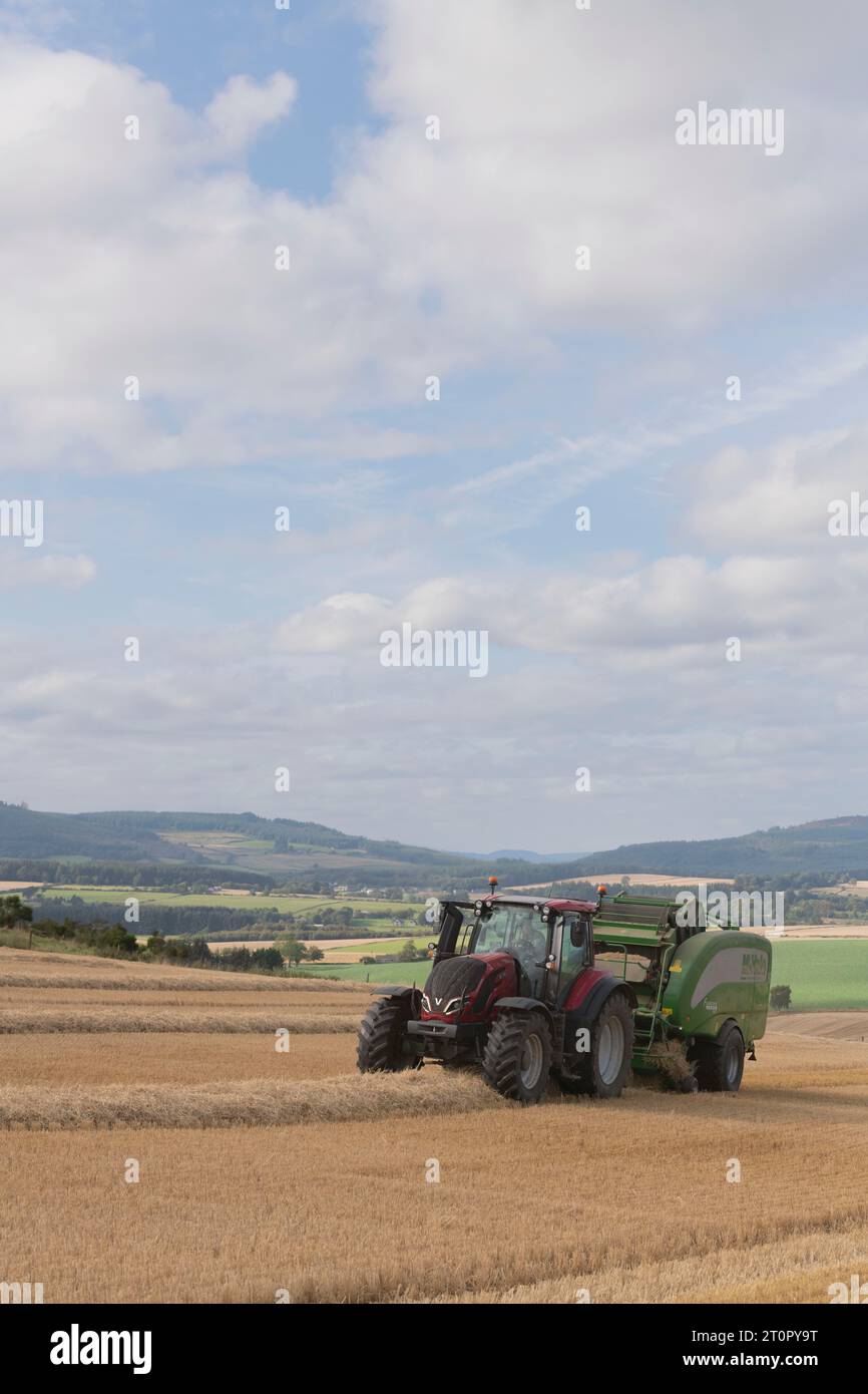 Imballaggio della paglia d'orzo con un trattore Valtra e una pressa McHale su terreni agricoli nell'Aberdeenshire Foto Stock