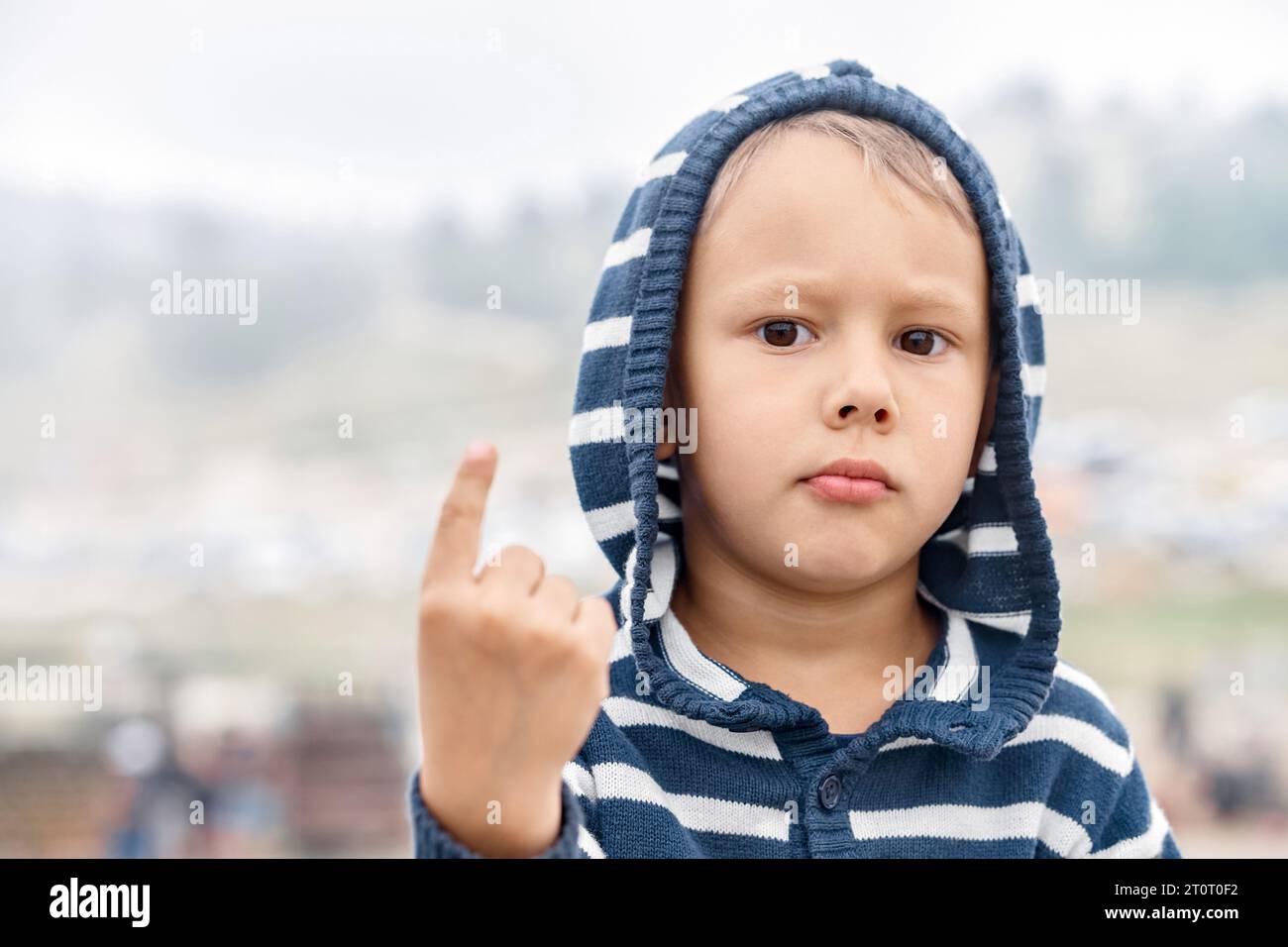 Il bambino serio mostra il dito diretto su uno sfondo sfocato all'aperto. Bambino in punti con cappuccio che cammina verso l'alto nel parco di montagna Foto Stock