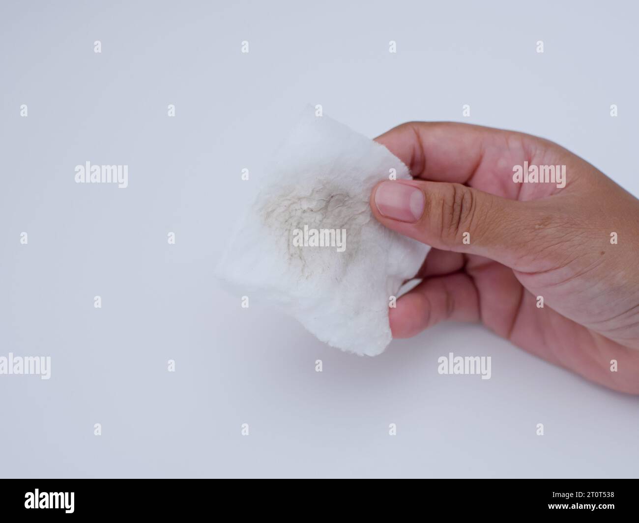 tenendo la mano si è usato un batuffolo di cotone sporco per pulire la faccia su sfondo bianco, eliminando il concetto di trucco Foto Stock