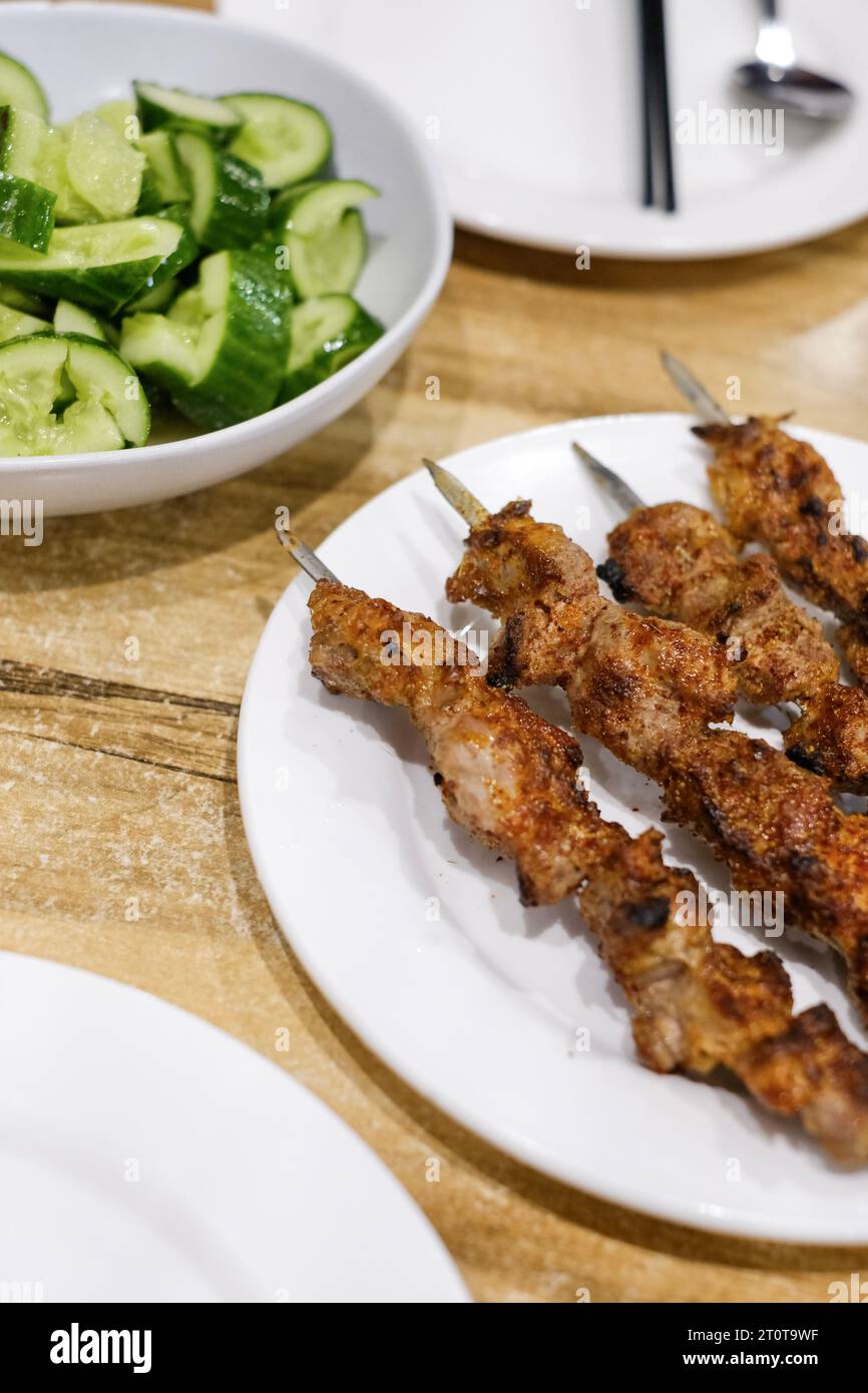 Un piatto di spiedini di agnello al cumino e contorno di insalata di cetrioli all'aglio al ristorante Appandim Uyghur a Burwood - Sydney, NSW, Australia Foto Stock