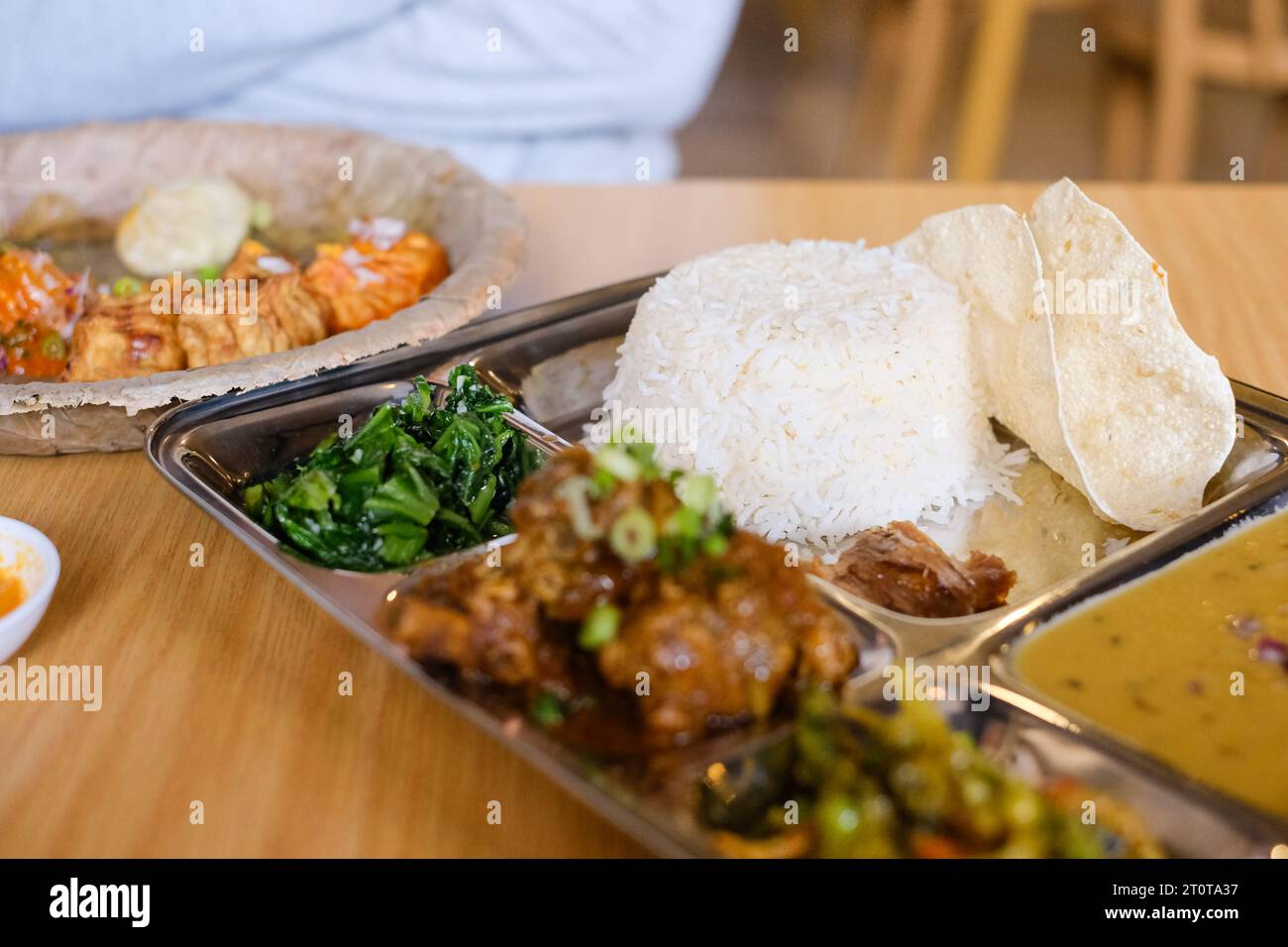 Alimentazione baht con daal di pollo (riso, spinaci, lenticchie, sottaceti e curry di pollo) servita su un vassoio di acciaio inossidabile in un ristorante nepalese a Sydney Foto Stock