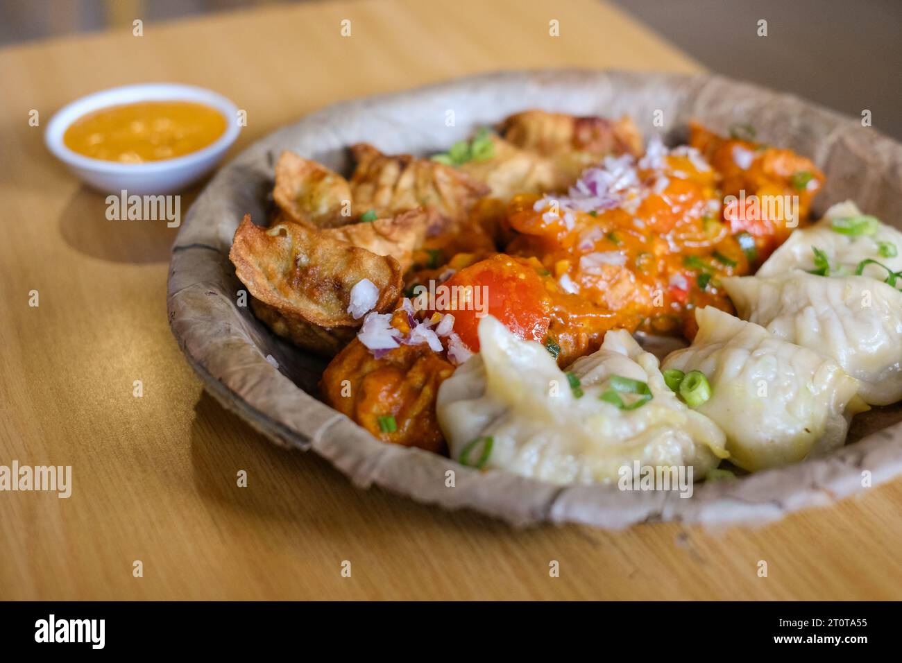 Un piatto di mamme di pollo assortite (gnocchi al vapore, fritti e salsa al peperoncino) servito su un piatto di foglie al Tapari Nights, un ristorante nepalese a Sydney Foto Stock