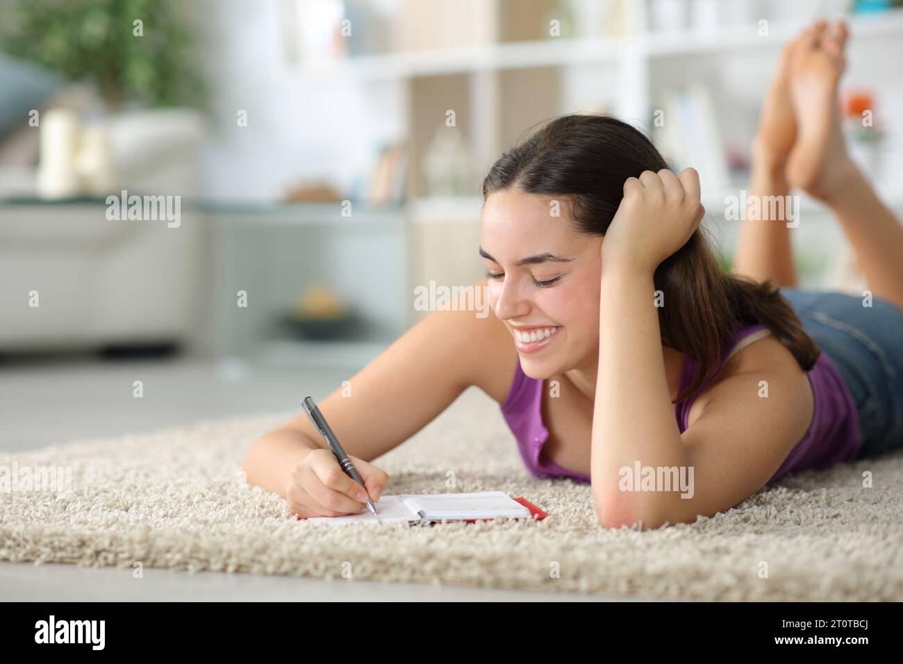 Donna felice che prende appunti all'ordine del giorno sdraiata su un tappeto a casa Foto Stock