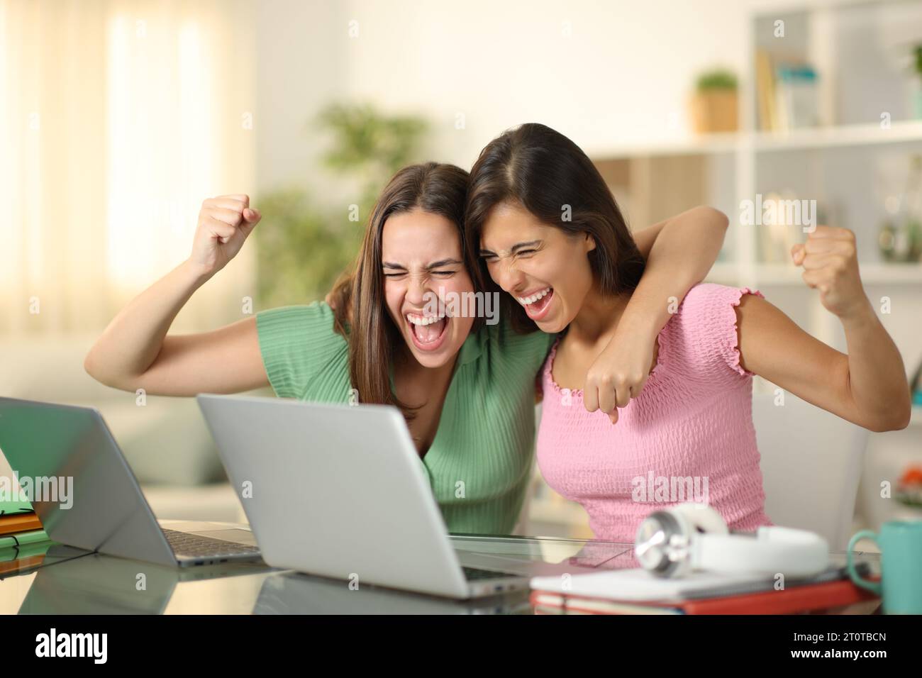 Studenti felici che festeggiano il successo insieme controllando il notebook a casa Foto Stock