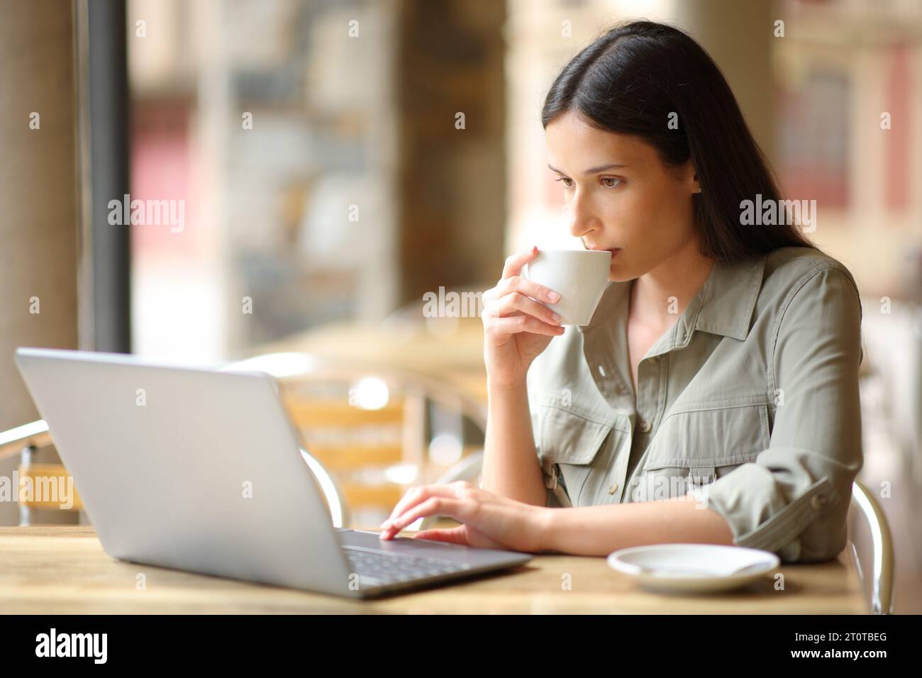 Donna che beve caffè e controlla il computer portatile in una terrazza del bar Foto Stock