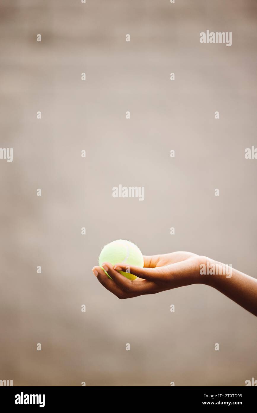 Primo piano di una tennista nera che tiene una palla da tennis gialla. Giocatore di tennis che cattura una palla con una mano mentre gioca una partita. Foto Stock