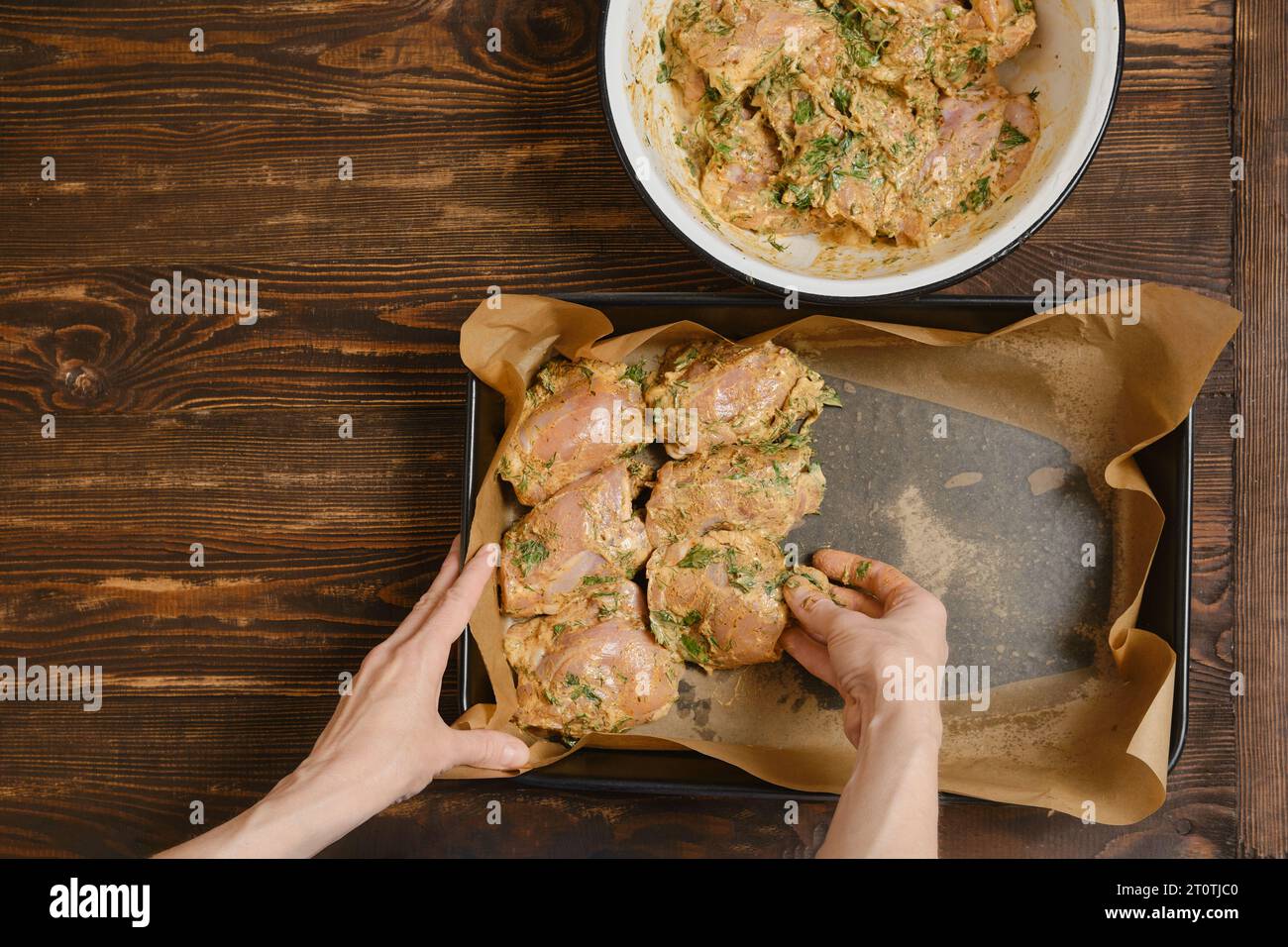 Mani di una donna che mette le cosce di pollo nel vassoio da forno di una ciotola Foto Stock