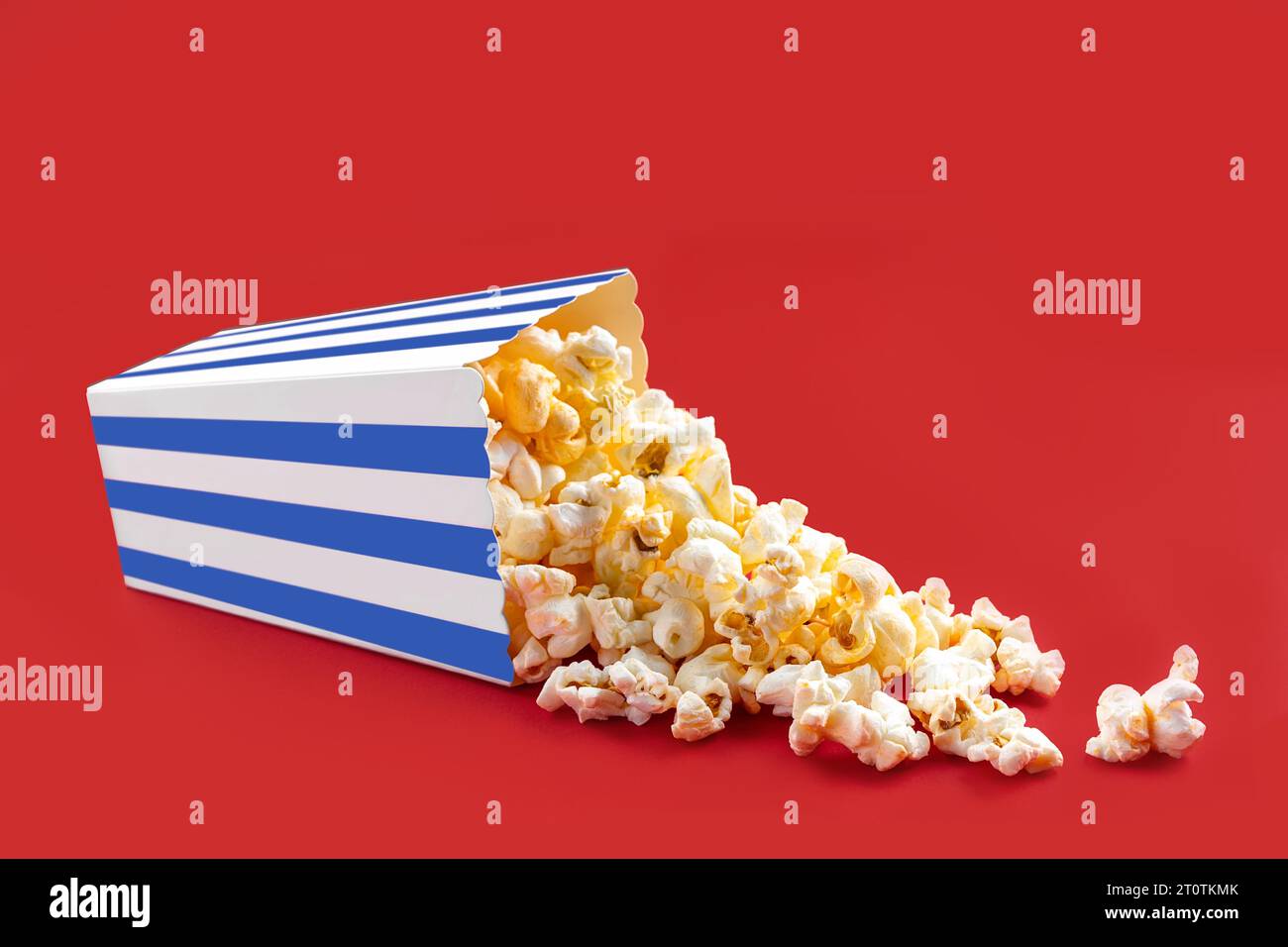 Gustosi popcorn al formaggio che cadono da una scatola di cartone a righe blu o da un secchio, isolato su sfondo rosso. Dispersione di semi di popcorn. Fast food, snack. M Foto Stock