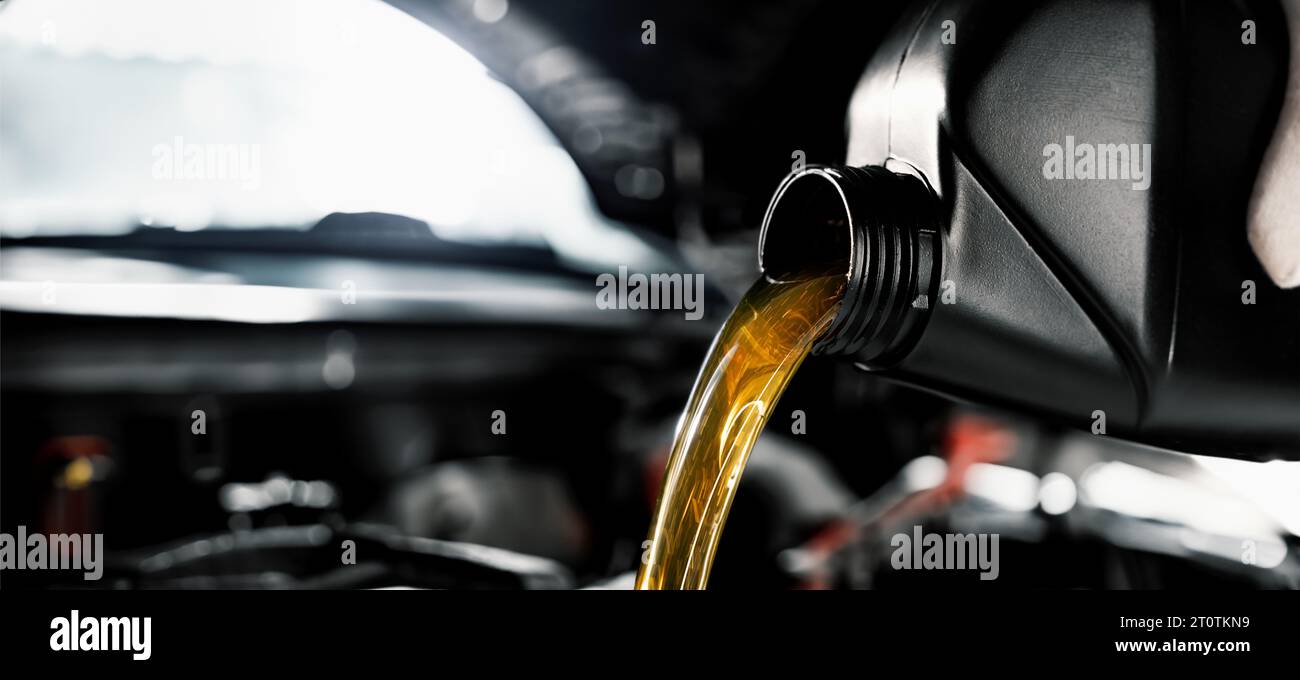 il meccanico versa olio motore dalla bottiglia nel motore presso un'officina di riparazione. striscione con spazio per la copia Foto Stock